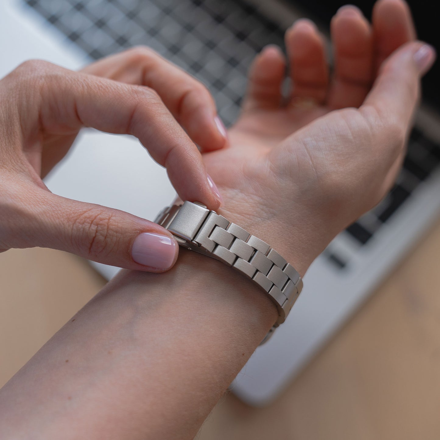Eine Person befestigt das Arktisband Apple Watch Gliederarmband „Arctica“ – Slim an ihrem linken Handgelenk vor einer Laptoptastatur.