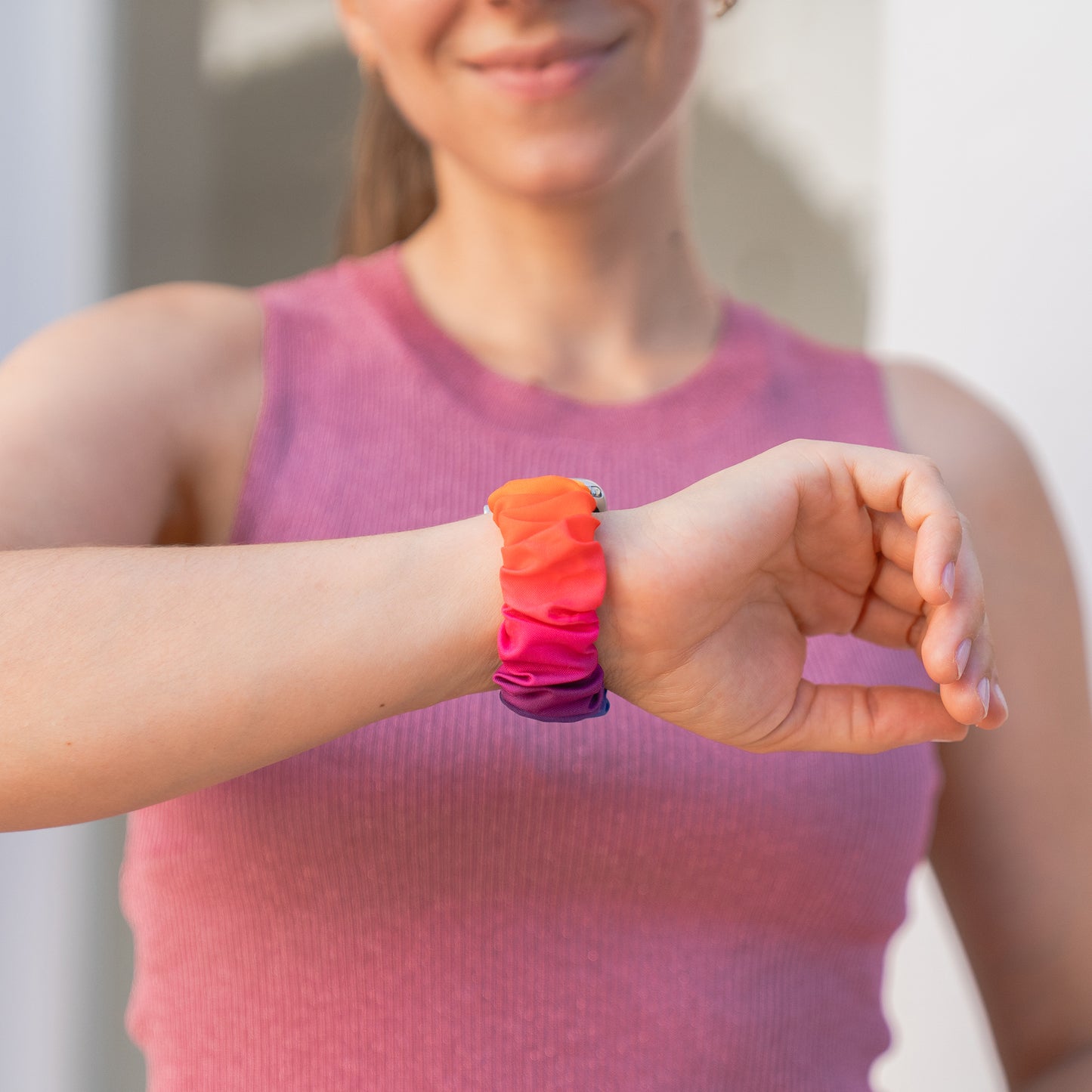 Eine Frau trägt ein rosa Oberteil und das Arktisband Apple Watch Scrunchie Armband "Elanora" am Handgelenk und lächelt.