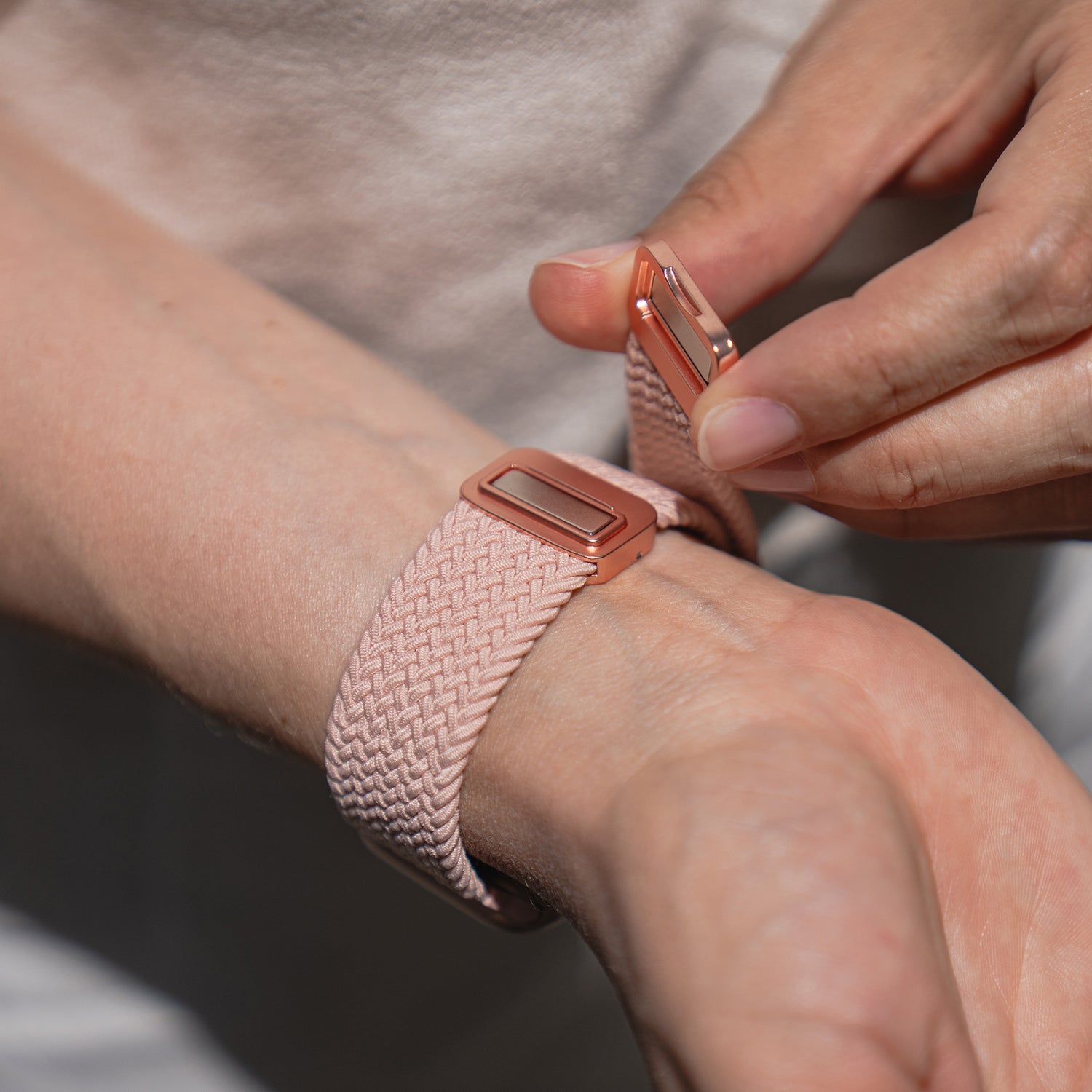 Eine Person befestigt ein arktisband Geflochtenes Apple Watch Armband „Casual“ mit einem roségoldenen Magnetverschluss an ihrem Handgelenk.