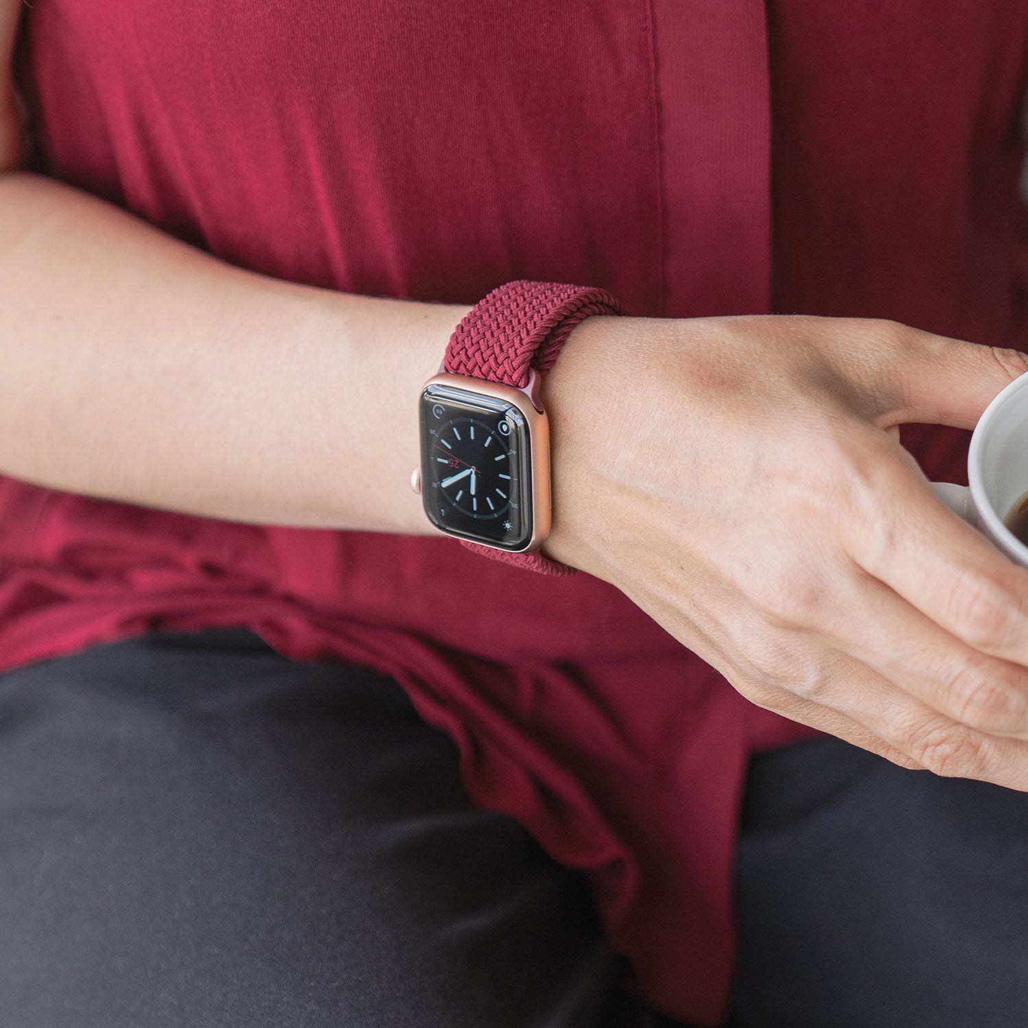 Eine Person trägt ein von Arktisband geflochtenes Apple Watch Armband „Casual“ mit Magnetverschluss in Rot, hält eine kleine weiße Tasse und ist mit einem roten Oberteil bekleidet.