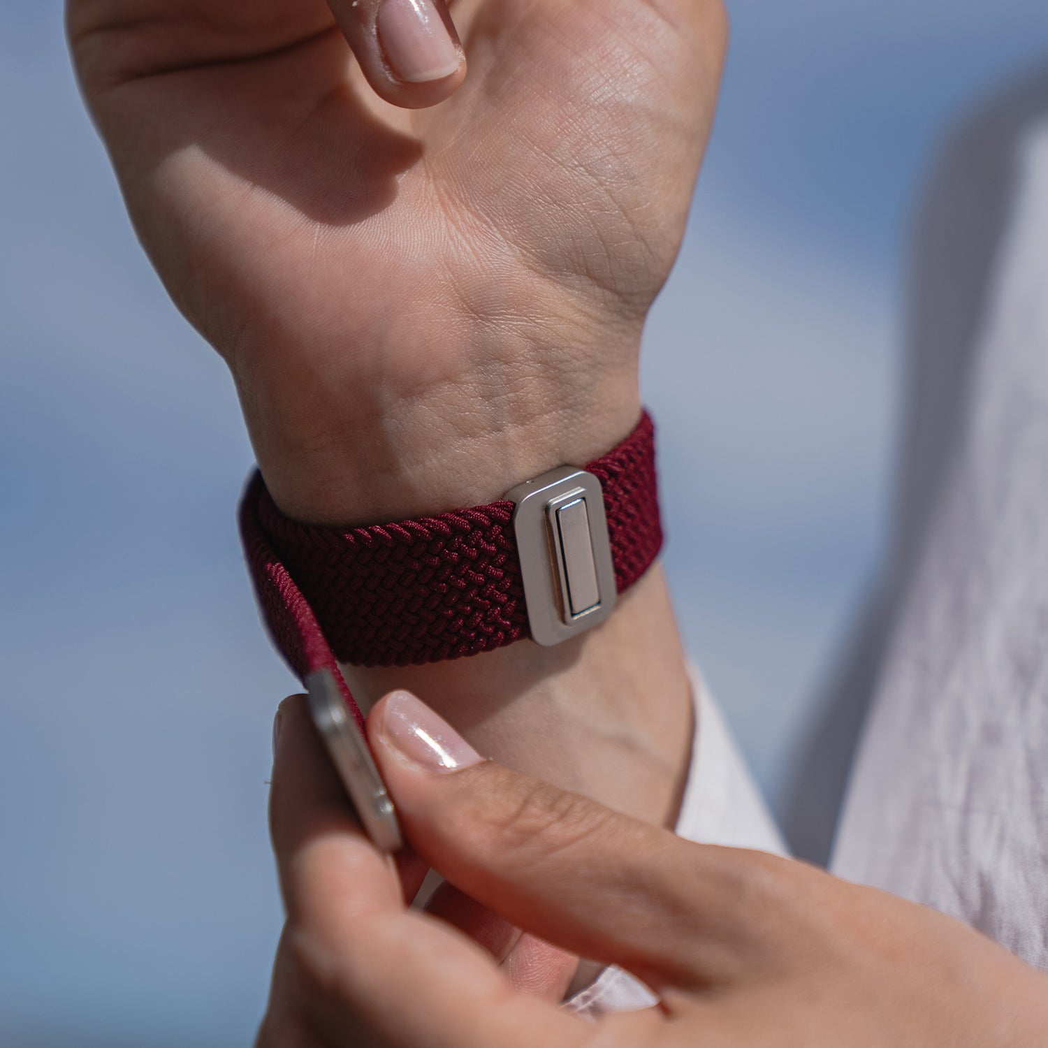 Befestigung des Arktisband Geflochtenen Apple Watch Armbands „Casual“ mit Magnetverschluss in Kastanienbraun, mit einem eleganten silbernen Magnetverschluss auf verschwommenem blauem Hintergrund.