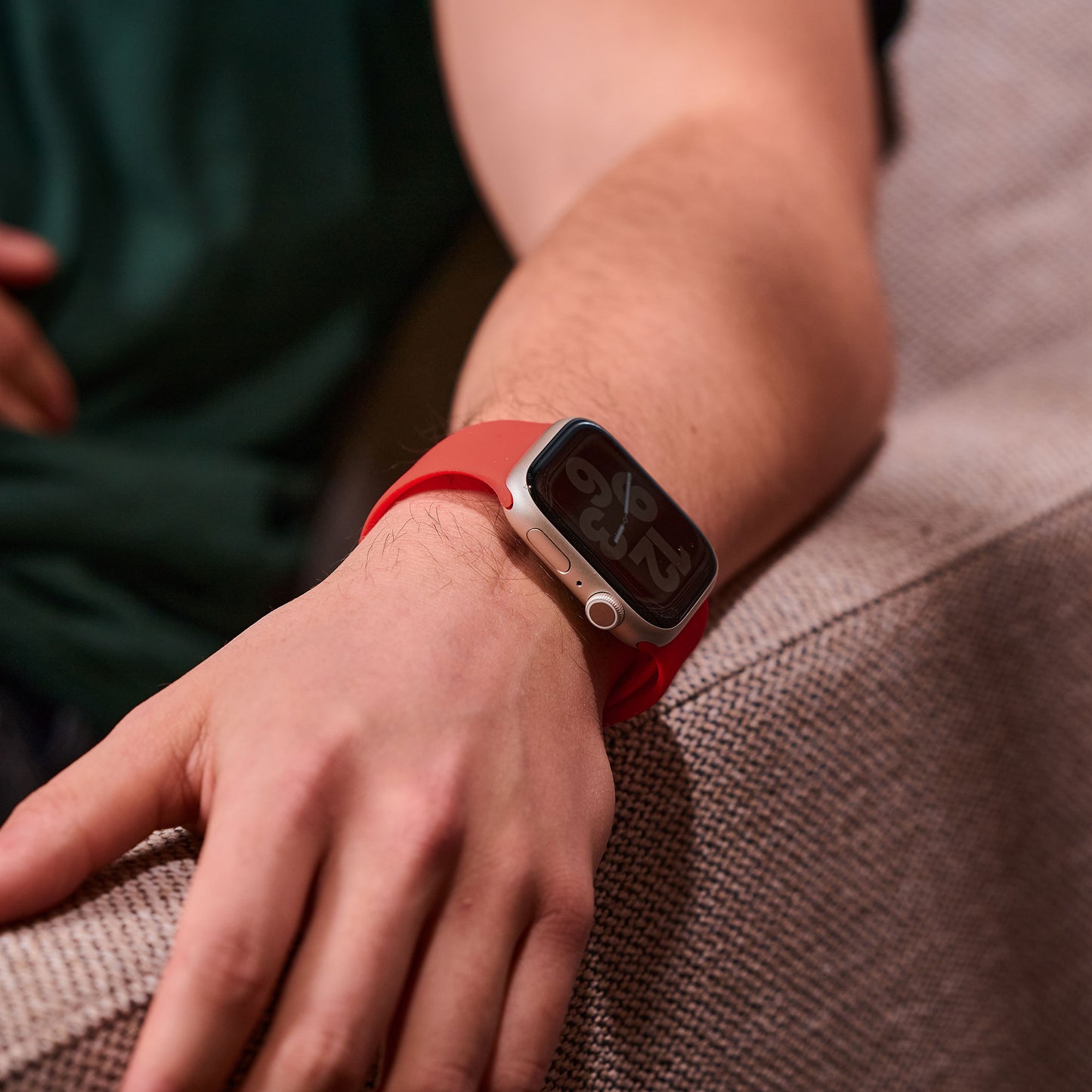 Eine Person in einem dunkelgrünen Hemd ruht mit dem Arm auf einem beigefarbenen Sofa. Sie trägt ein arktisband Apple Watch Silikonarmband „Aqua“ von arktisband. Das Display der Smartwatch ist sichtbar und zeigt die Uhrzeit an.