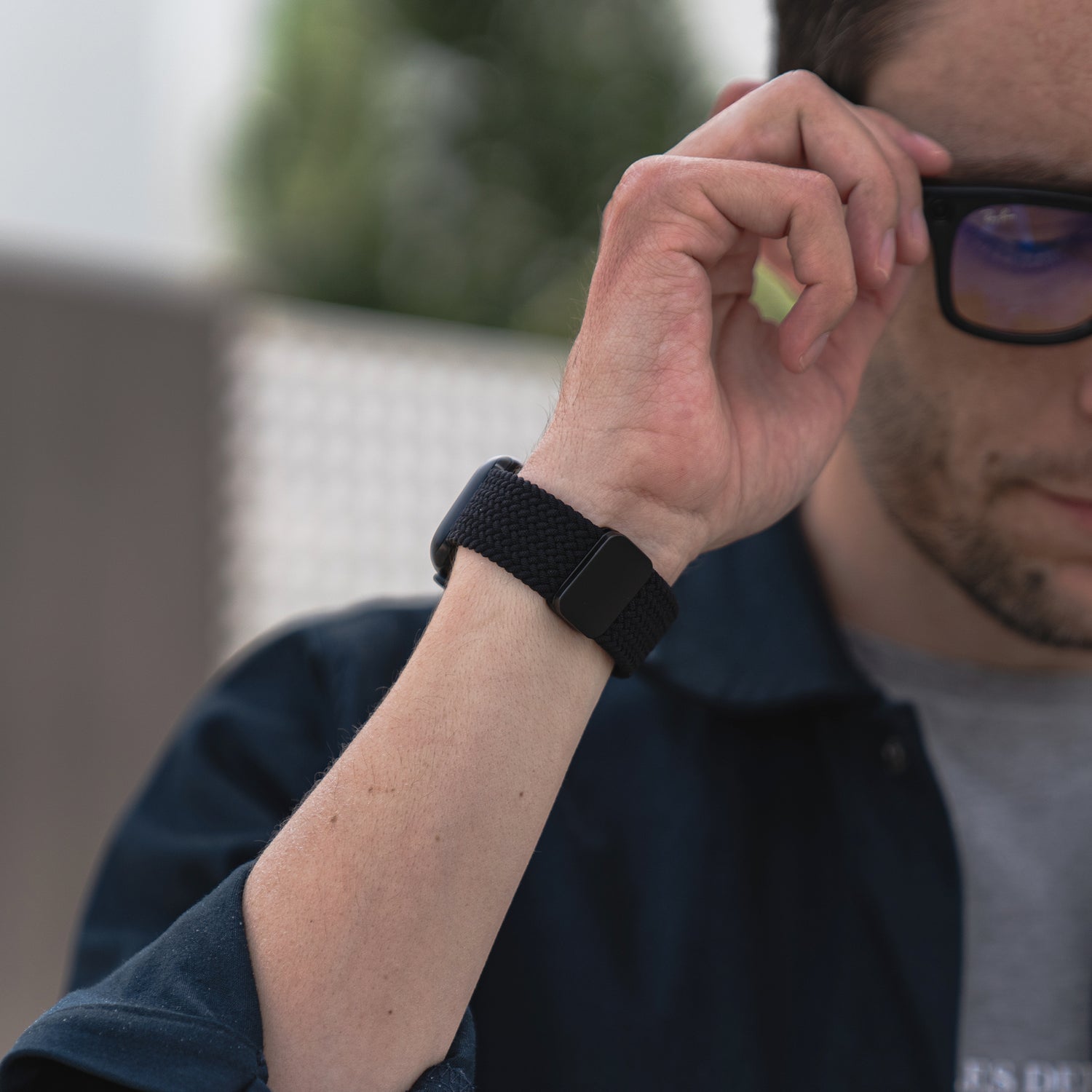 Im Freien rückt eine Person ihre Brille zurecht, während sie ein arktisband Geflochtenes Apple Watch Armband „Casual“ mit Magnetverschluss von arktisband am Handgelenk trägt.