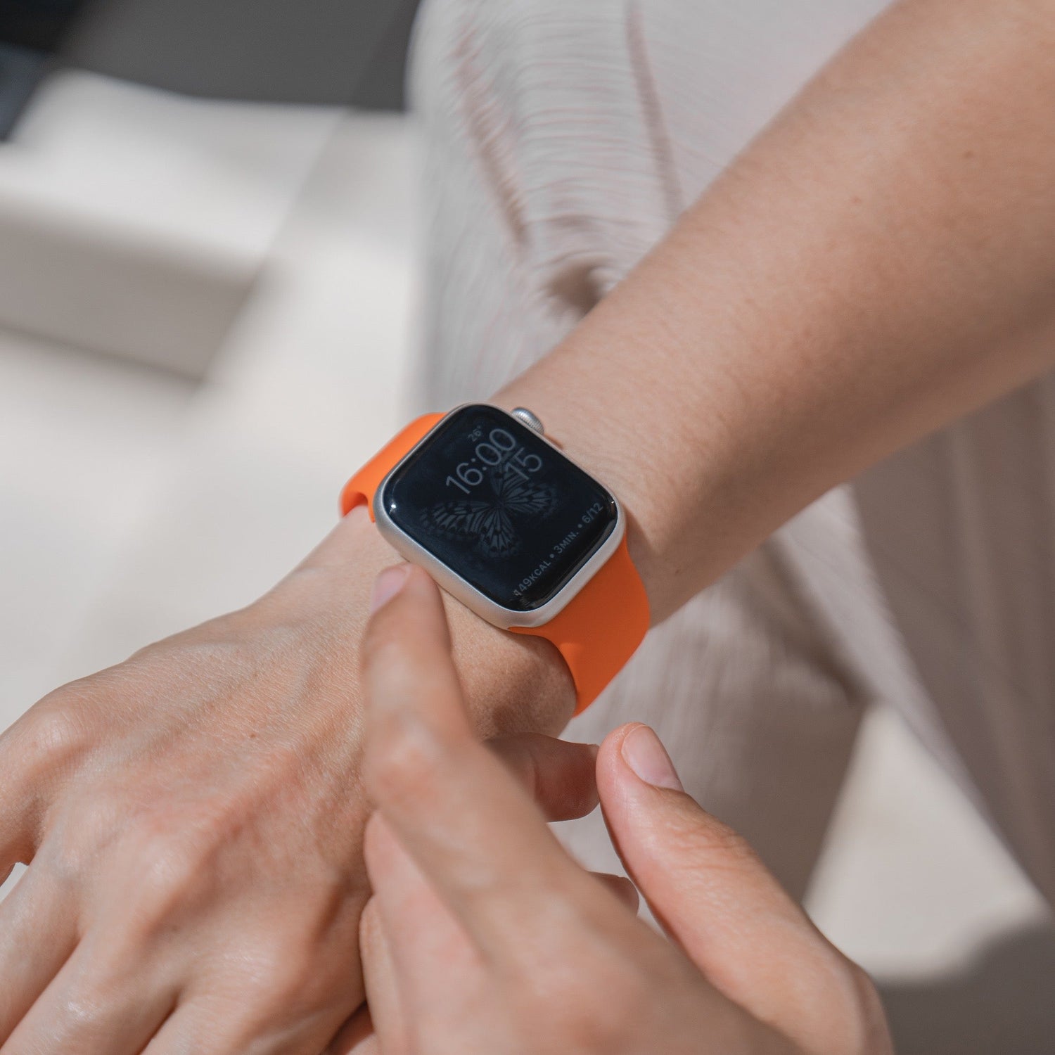 Person trägt eine orangefarbene Smartwatch und interagiert mit dem Bildschirm, der die Uhrzeit 16:00 anzeigt.