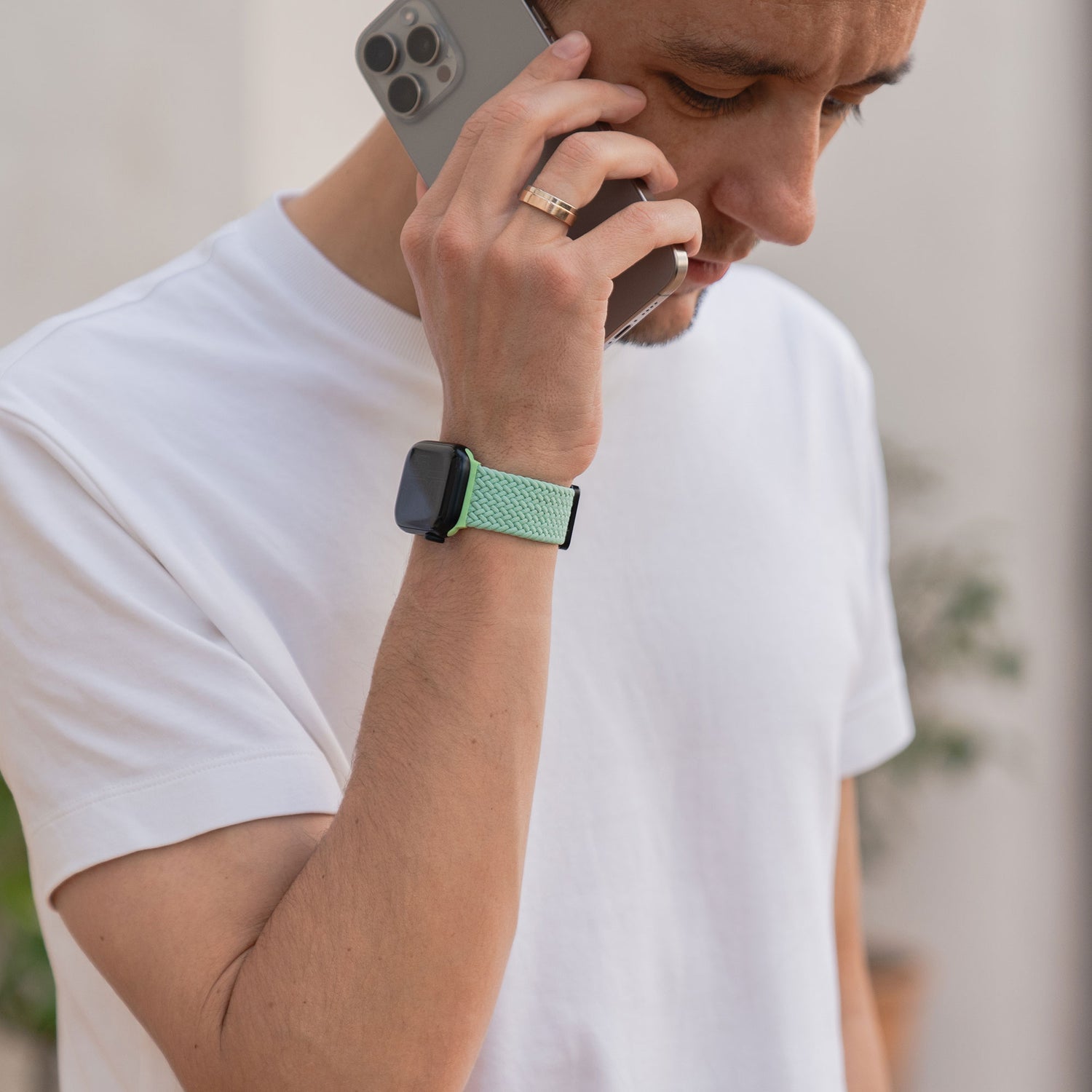 Ein Mann im weißen T-Shirt telefoniert mit seinem Smartphone und trägt ein arktisband Geflochtenes Apple Watch Armband „Casual“ mit Magnetverschluss in Grün am Handgelenk.