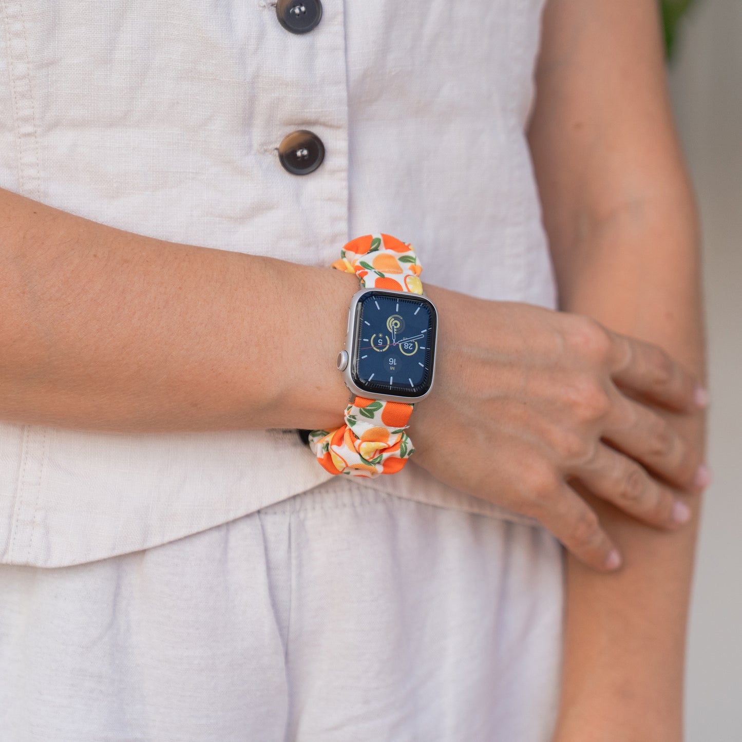 Nahaufnahme einer Person, die das arktisband Apple Watch Scrunchie Armband "Elanora" trägt, mit einem farbenfrohen, orange gemusterten Gummiband von arktisband für einen stilvollen, komfortablen Look.