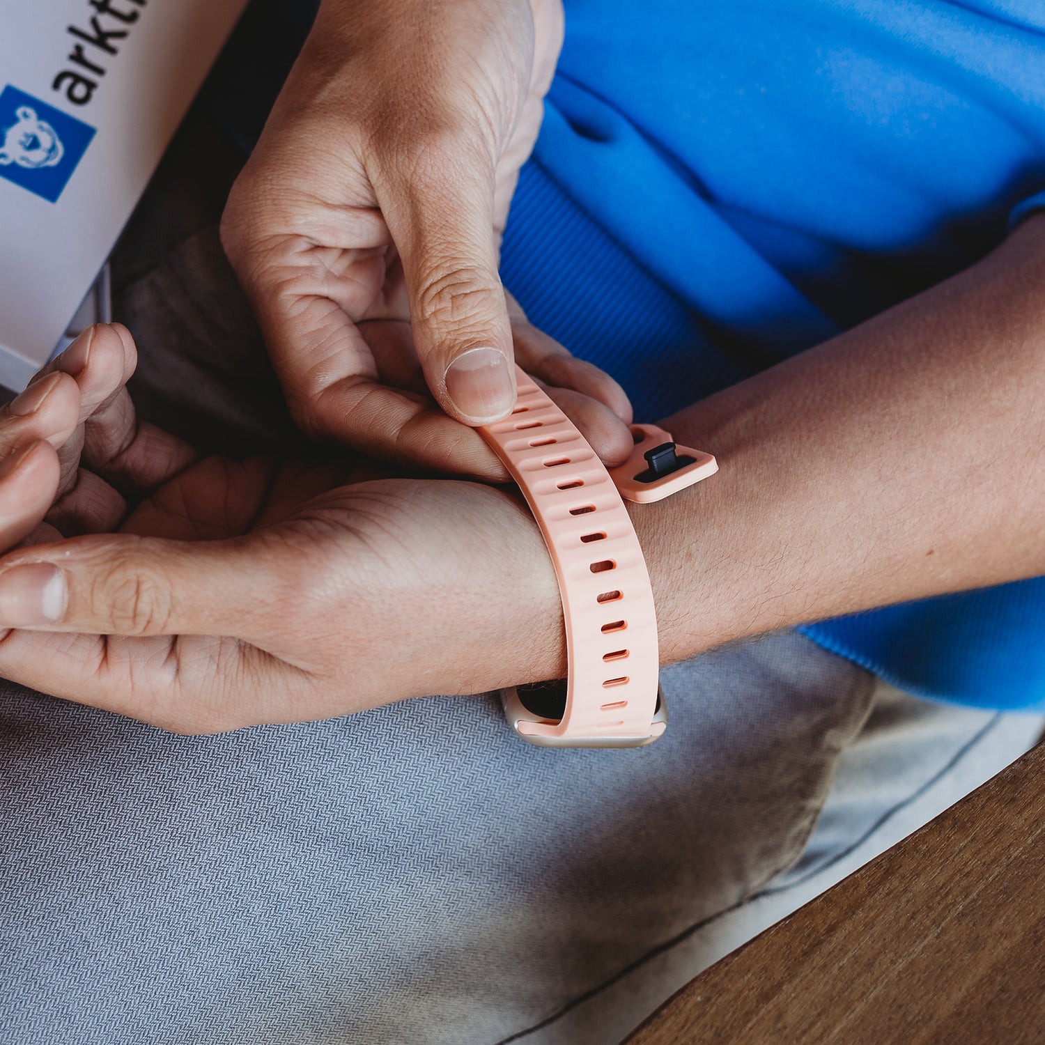 Eine Person in einem blauen Hemd befestigt an einem Tisch sitzend ein Arktisband Apple Watch Silikonarmband „Active“ am Handgelenk.