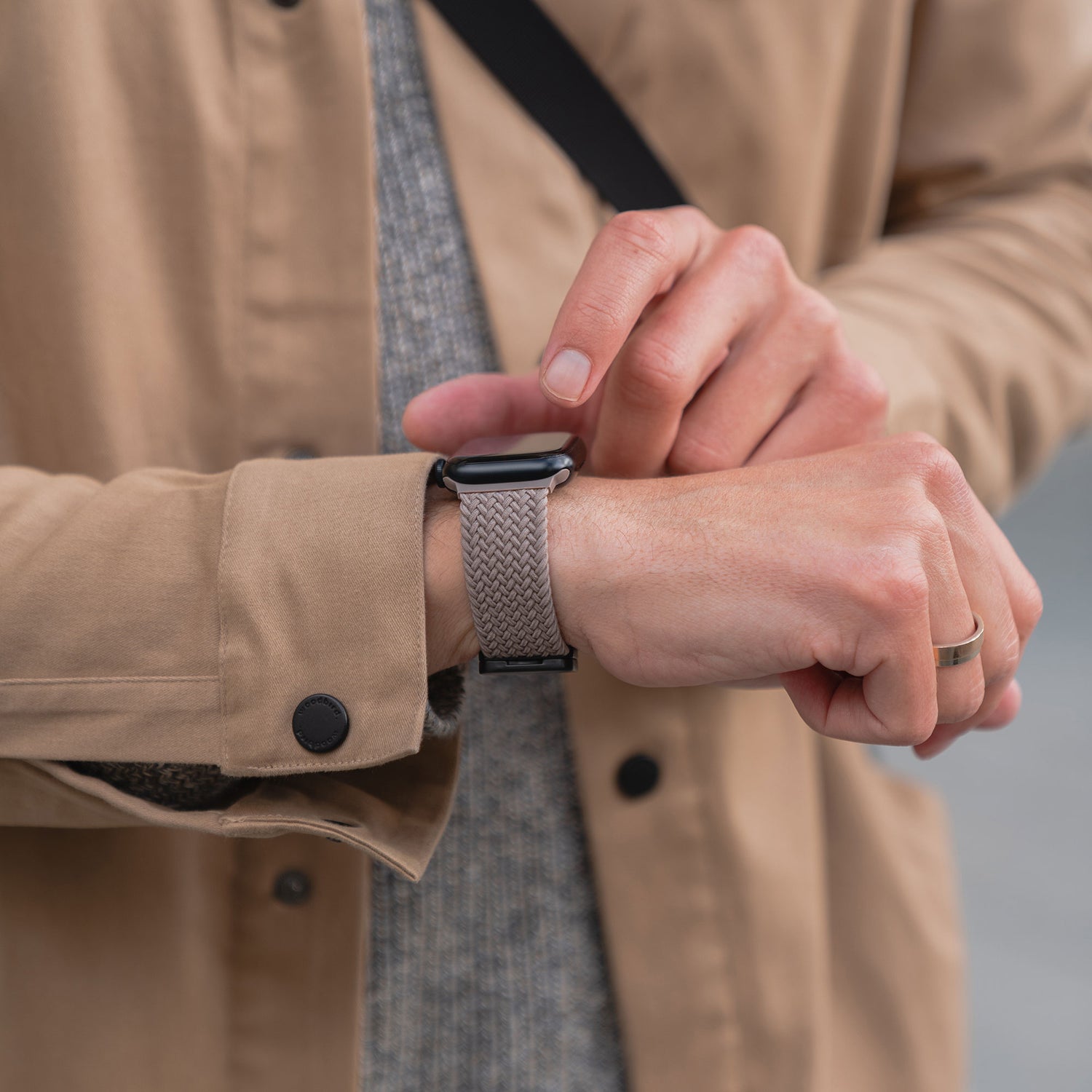 Eine Person in einem braunen Mantel passt ihr arktisband Geflochtenes Apple Watch Armband „Casual“ mit Magnetverschluss von arktisband an.