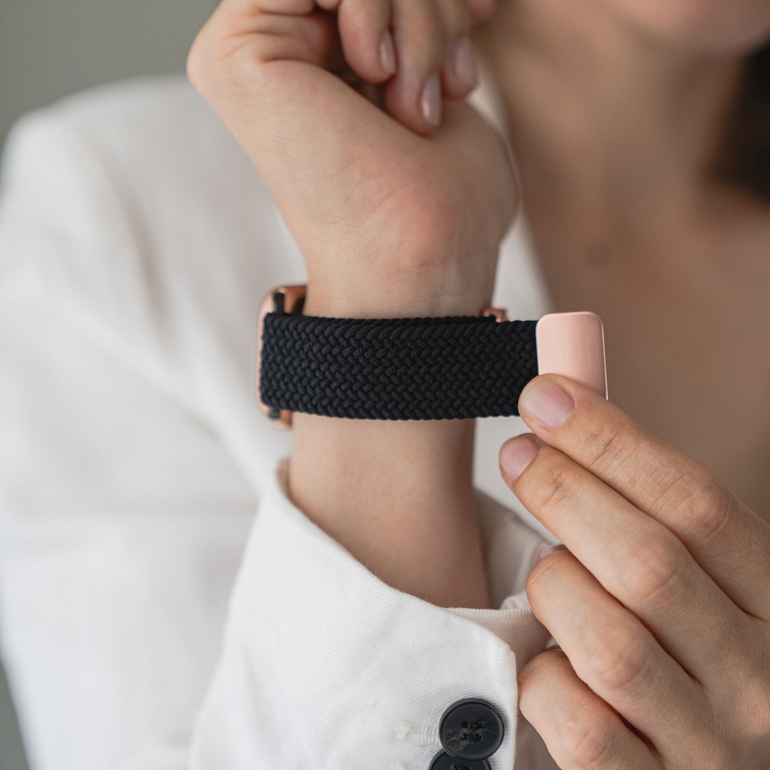 Eine Person legt das geflochtene Apple Watch Armband „Casual“ mit Magnetverschluss von Arktisband an ihr Handgelenk und kombiniert es mit einem weißen Langarmshirt.