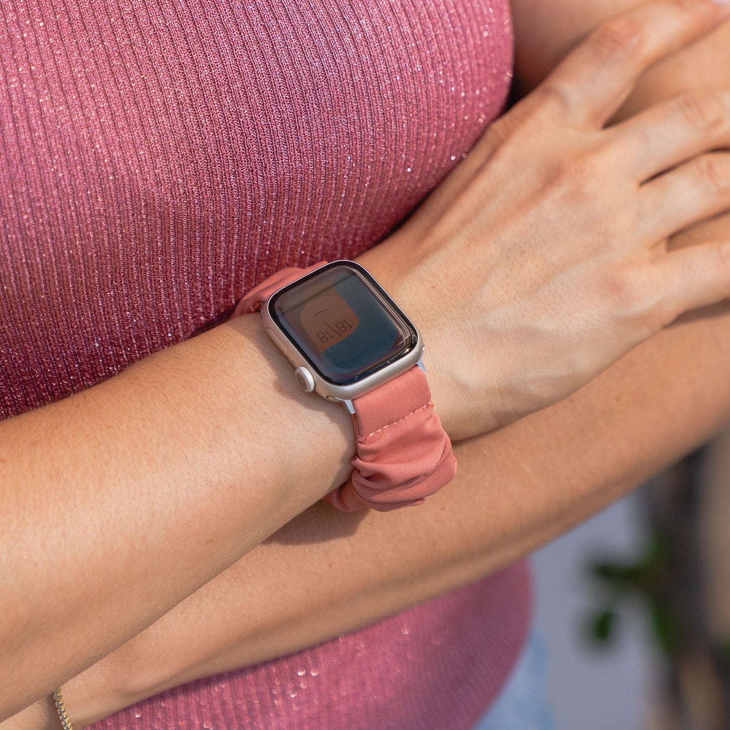 Eine Person, die ein rosa Arktisband Apple Watch Scrunchie Armband "Elanora" trägt, steht mit verschränkten Armen in einem rosa Top.