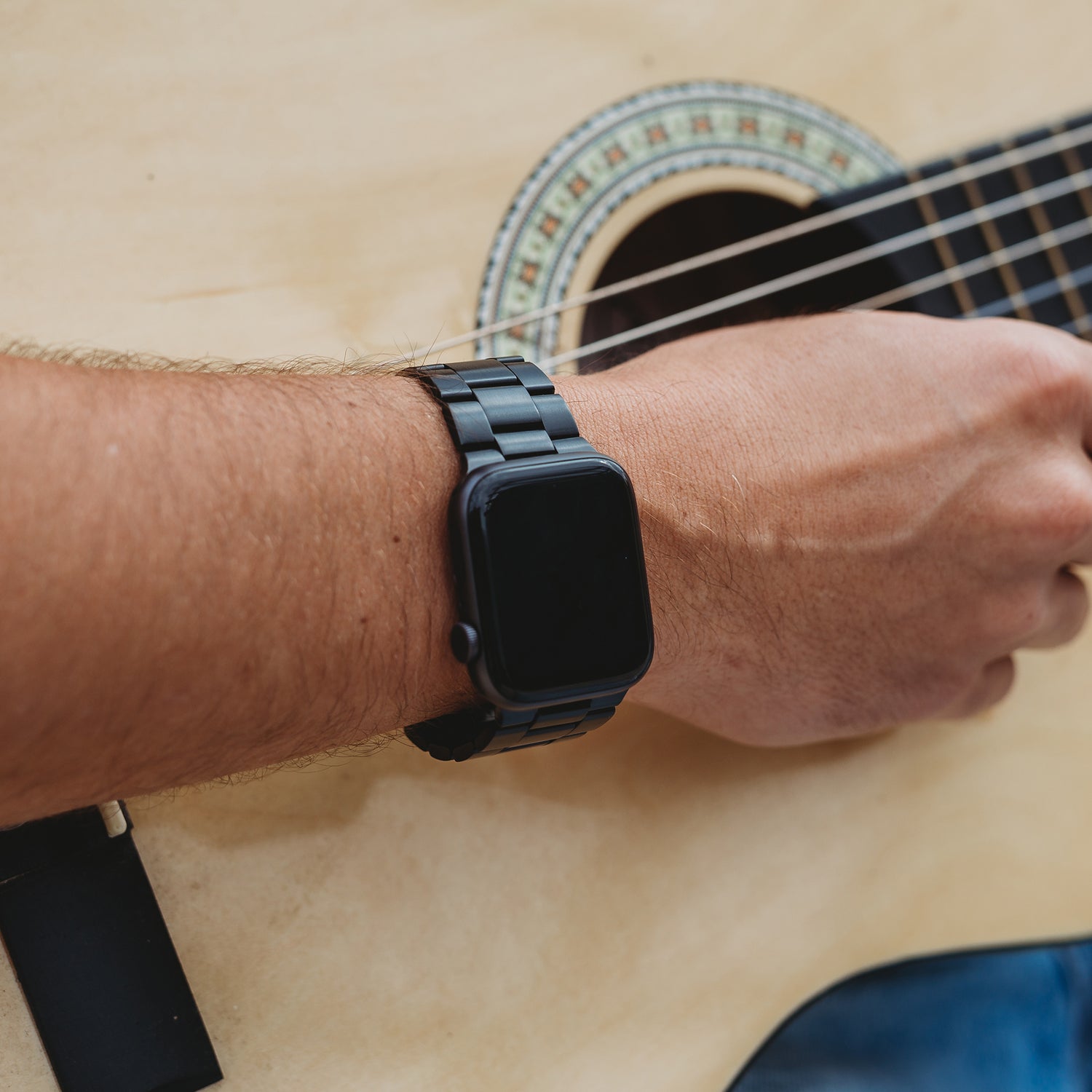 Jemand, der das Arktisband Apple Watch Gliederarmband „Prime“ trägt, klimpert auf einer Akustikgitarre, wobei seine Hand auf den Saiten in der Nähe des Schalllochs liegt.