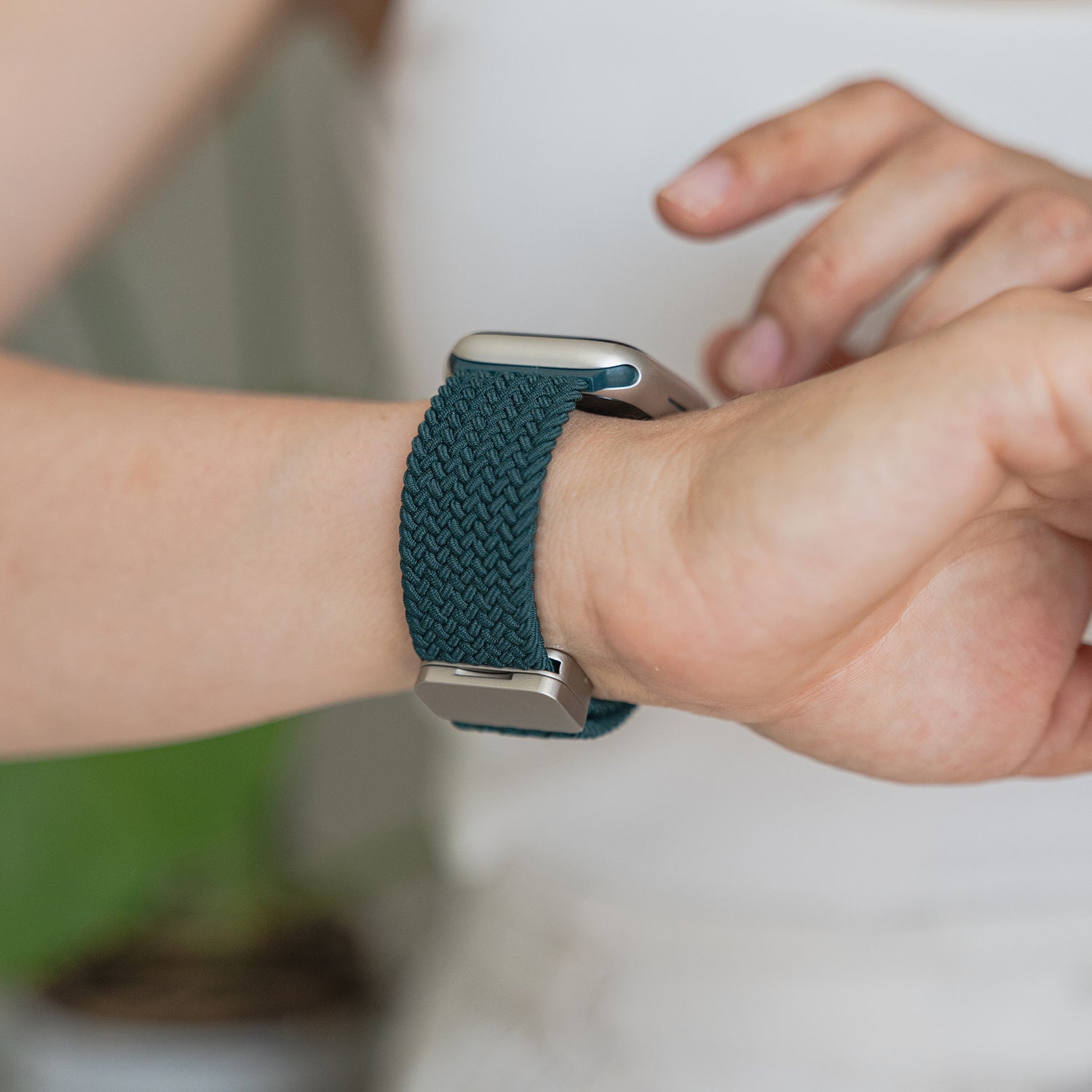 Eine Person trägt ein arktisband Geflochtenes Apple Watch Armband „Casual“ mit Magnetverschluss am Handgelenk und passt den Magnetverschluss mit der anderen Hand an.