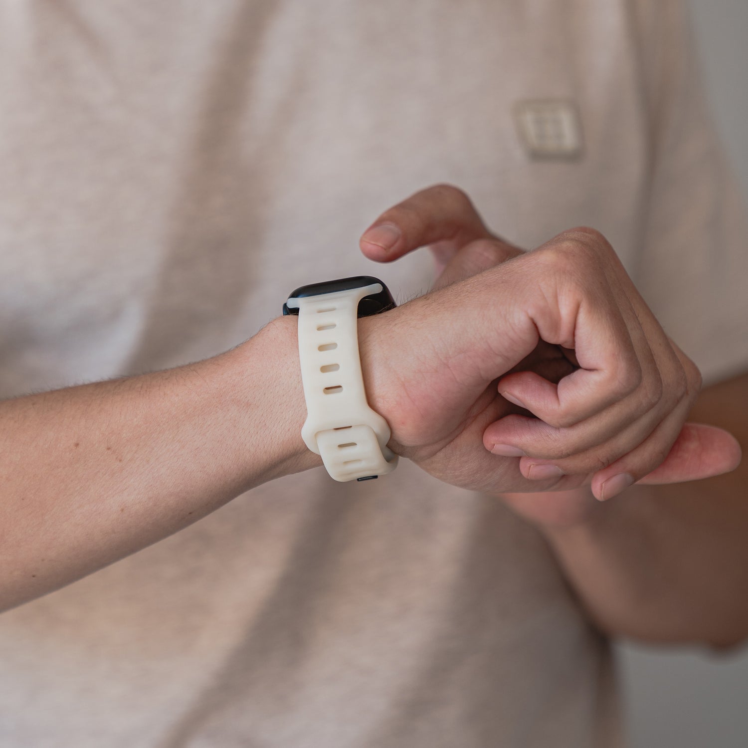 Eine Person in einem hellen Hemd berührt ihr links getragenes arktisband Apple Watch Silikonarmband „Active“ von arktisband, mit atmungsaktivem Design und weißem Silikonband.