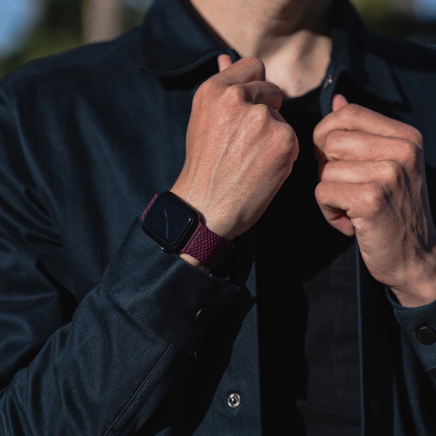 Person trägt eine dunkle Jacke und trägt am Handgelenk ein kunstvoll geflochtenes Apple Watch Armband „Casual“ mit Magnetverschluss in Lila.