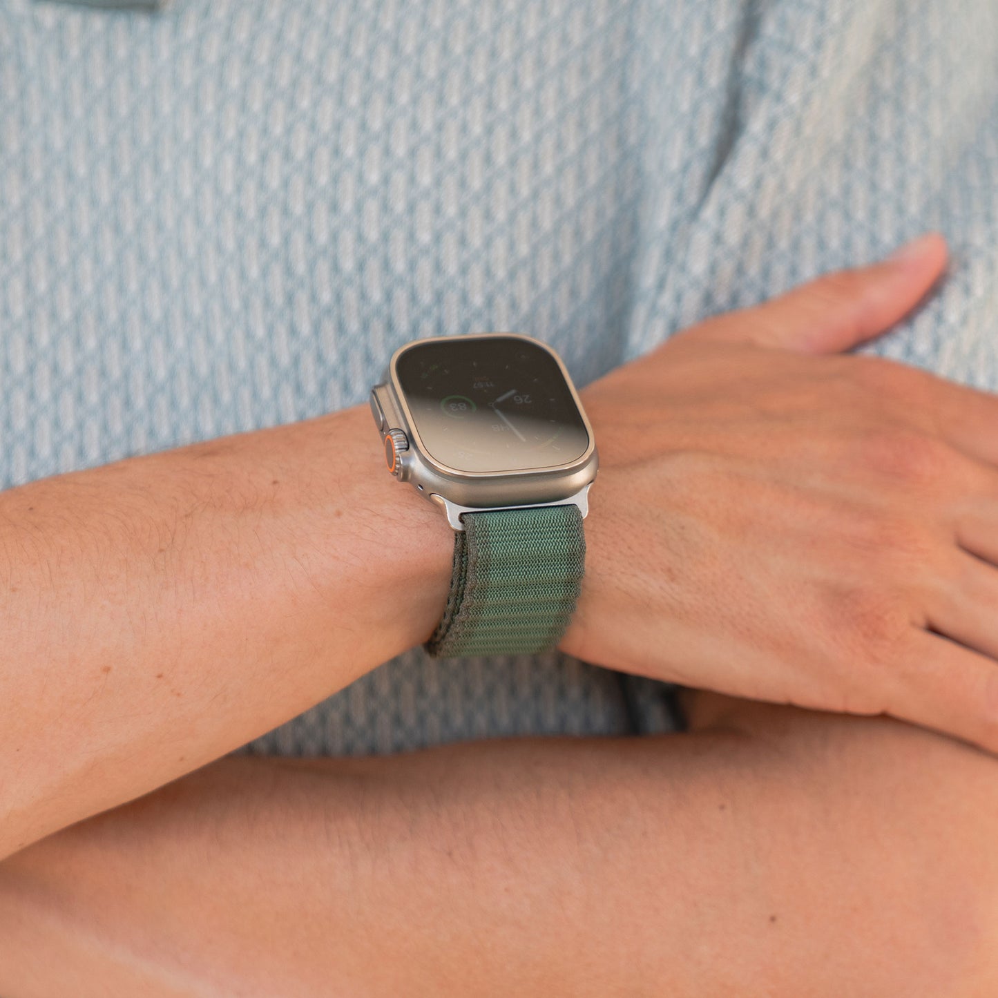 Der Träger des arktisband Apple Watch Nylonarmbands „Venture“ in Wave-Look Grün hat die Arme vor der Brust verschränkt und trägt dazu ein hellblaues gemustertes Shirt – ideal für Outdoor-Fans.