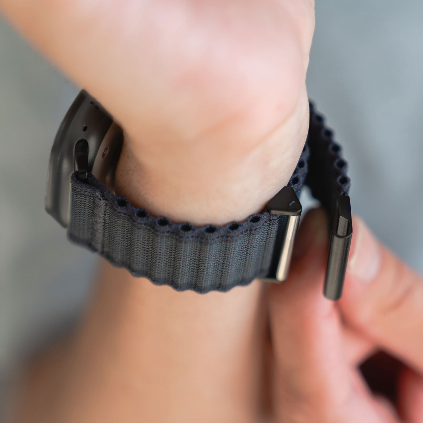 Eine Nahaufnahme zeigt jemanden, der das arktisband Apple Watch Nylonarmband „Venture“ um sein Handgelenk legt. Das Zifferblatt ist verdeckt und der Hintergrund unscharf – ideal für Outdoor-Enthusiasten, die Wert auf Stil und Funktionalität legen.