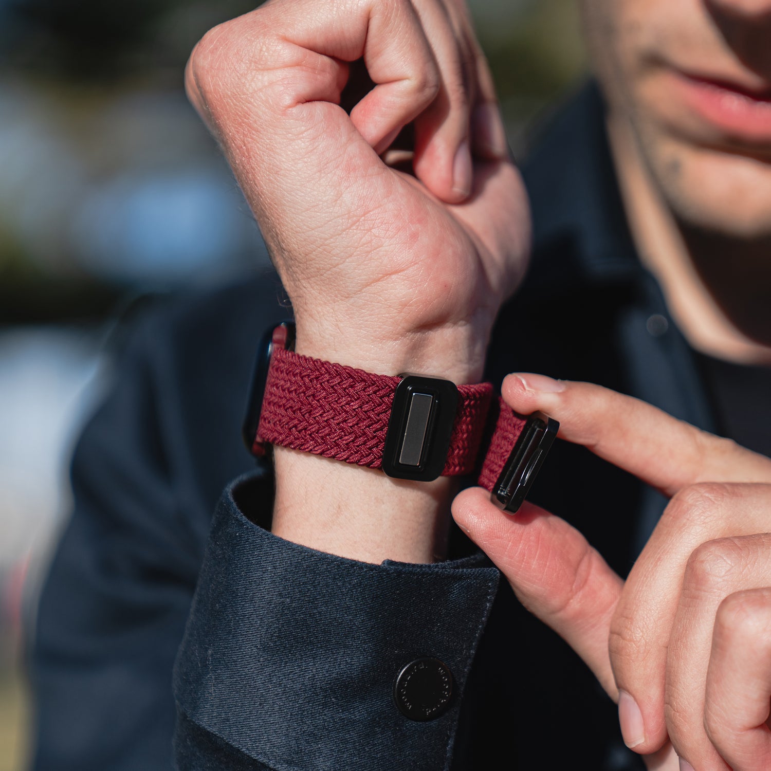 Eine Person befestigt ein arktisband Geflochtenes Apple Watch Armband „Casual“ mit Magnetverschluss von arktisband, in Rot mit schwarzem Magnetverschluss, an ihrem linken Handgelenk.
