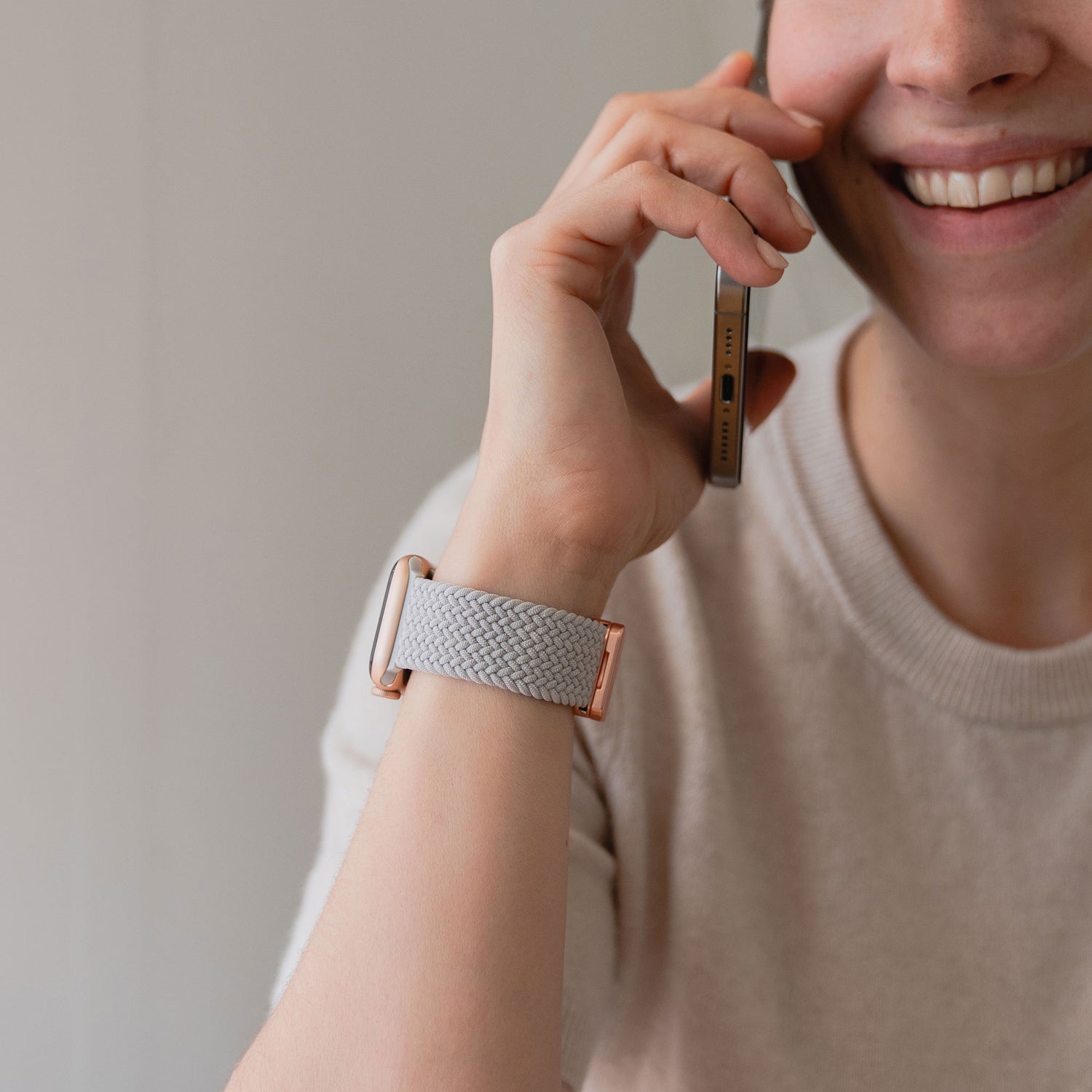 Lächelnde Person hält ein Smartphone in der Hand und trägt ein kunstvoll geflochtenes Apple Watch Armband „Casual“ mit Magnetverschluss am Handgelenk.