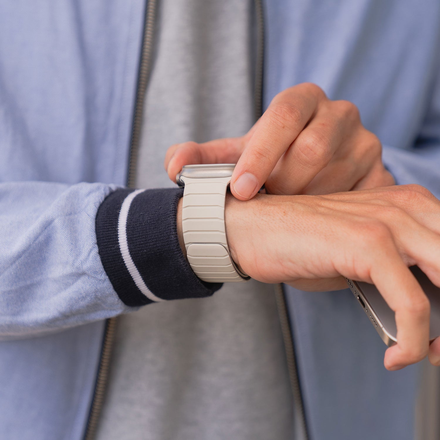 Nahaufnahme einer Person, die ihr magnetisches Armband „MagFlow“ für die Apple Watch von Arktisband an ihrem Handgelenk anpasst, während sie ein Smartphone hält. Dabei wird der magnetische Halt von Arktisband für zusätzliche Sicherheit und Komfort hervorgehoben.