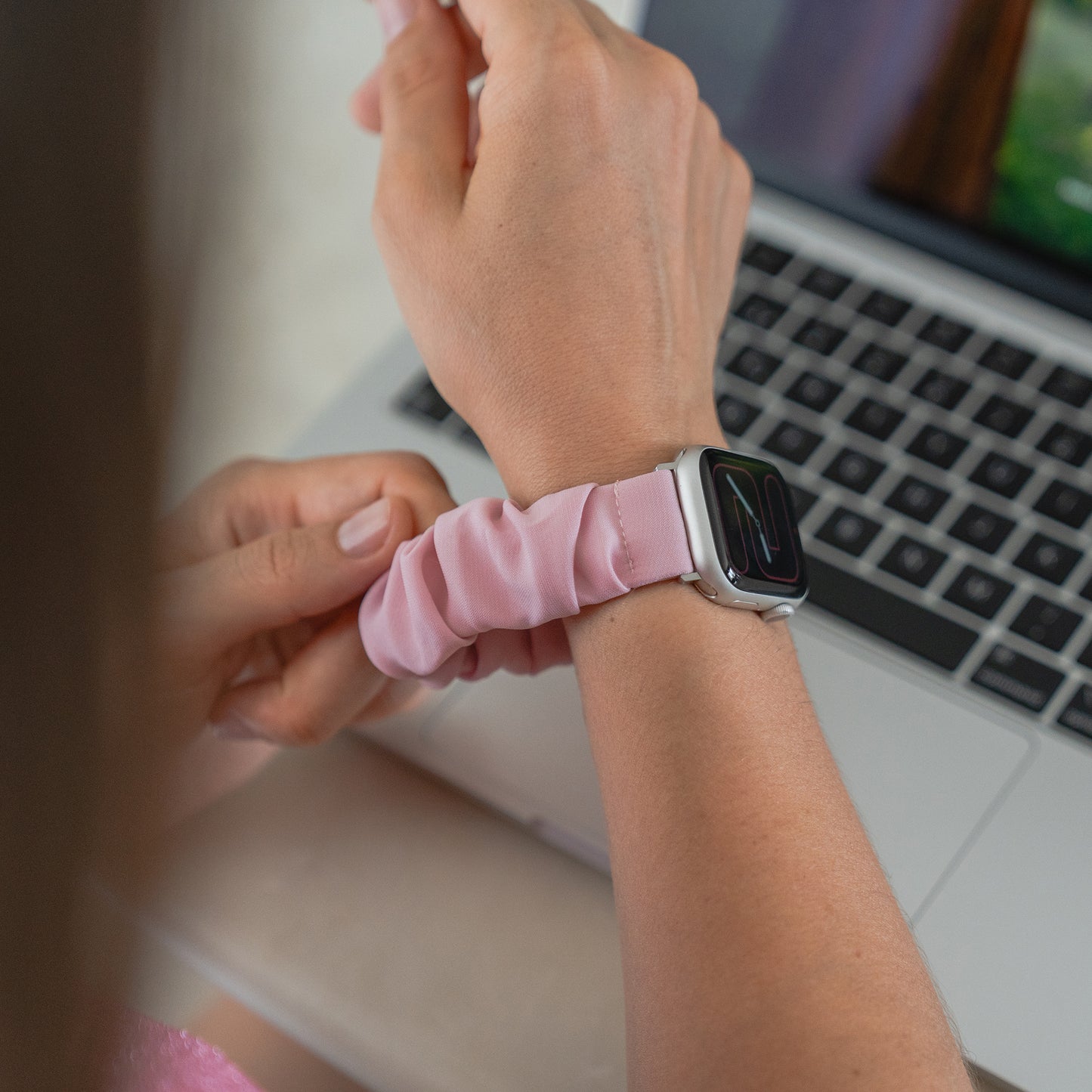 Jemand, der das arktisband Apple Watch Scrunchie Armband "Elanora" in Pink trägt, arbeitet an einem Laptop an einem Schreibtisch.