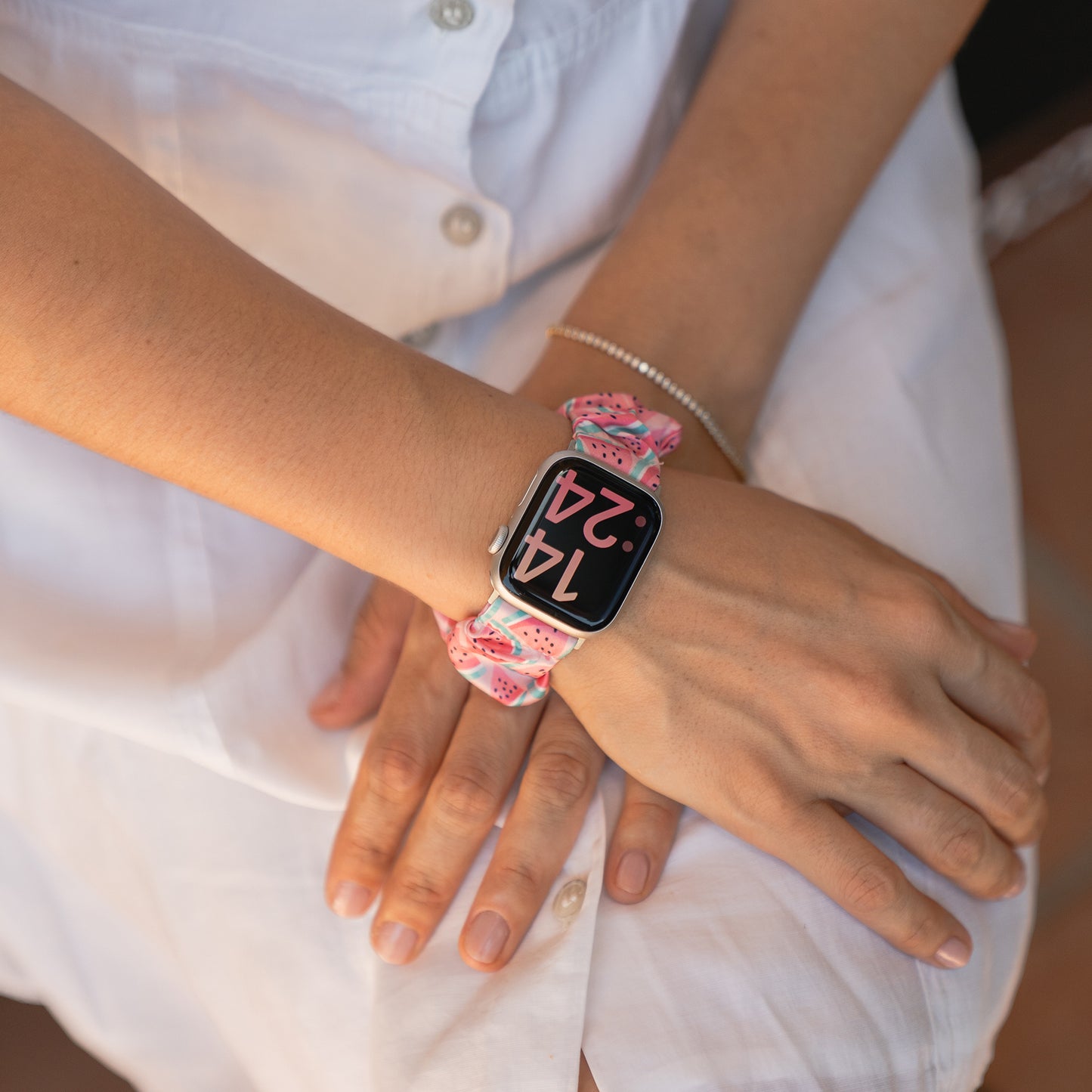 Jemand, der das arktisband Apple Watch Scrunchie Armband "Elanora" mit einem rosa gemusterten Gummiband trägt, legt die Hände auf den Schoß.