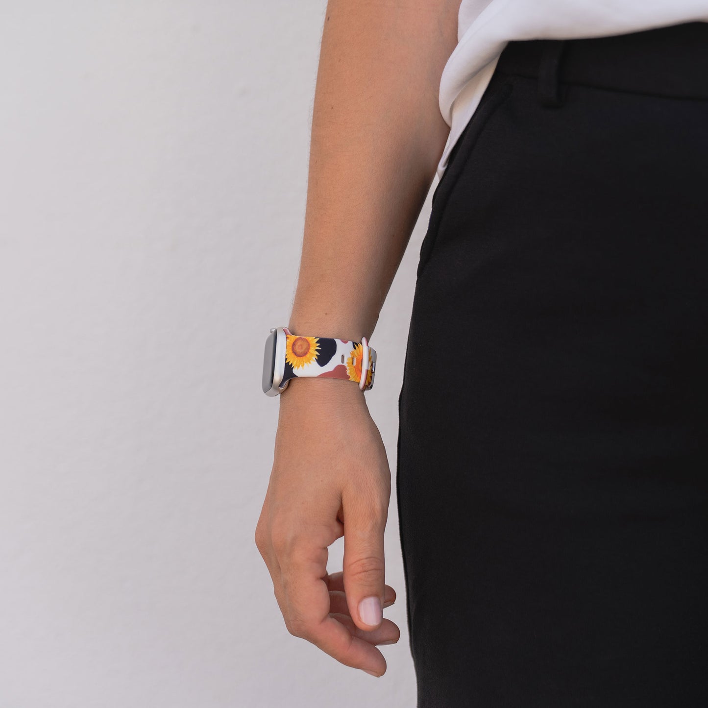 Eine Person, die eine schwarze Hose und eine arktisband EDITION für Apple Watch von arktisband mit einem Sonnenblumenmuster trägt, steht vor einer weißen Wand.