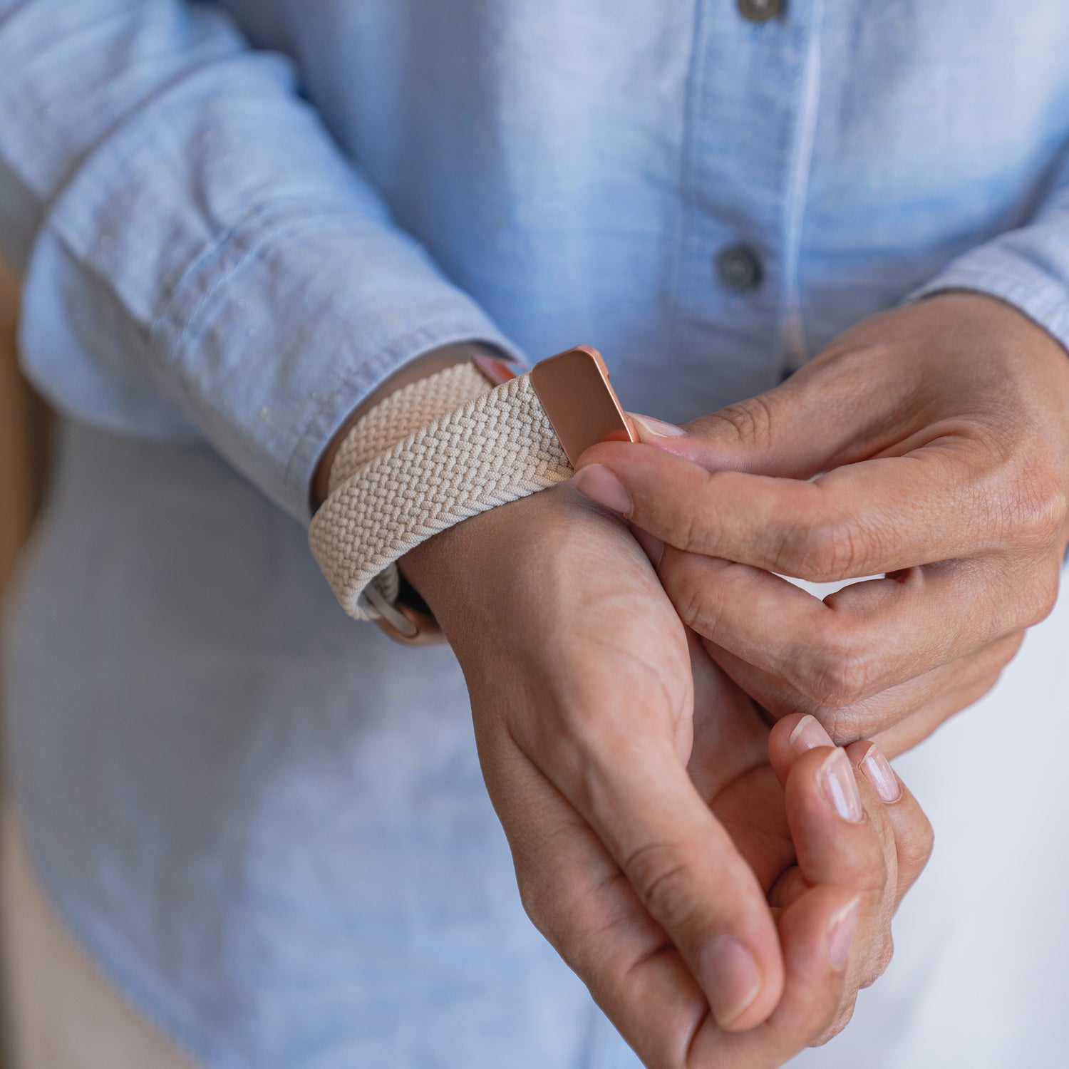 Eine Person in einem hellblauen Hemd befestigt ein arktisband Geflochtenes Apple Watch Armband "Casual" mit Magnetverschluss von arktisband in Beige am linken Handgelenk. Der Fokus liegt auf den Zeigern und dem geflochtenen Polyesterarmband.
