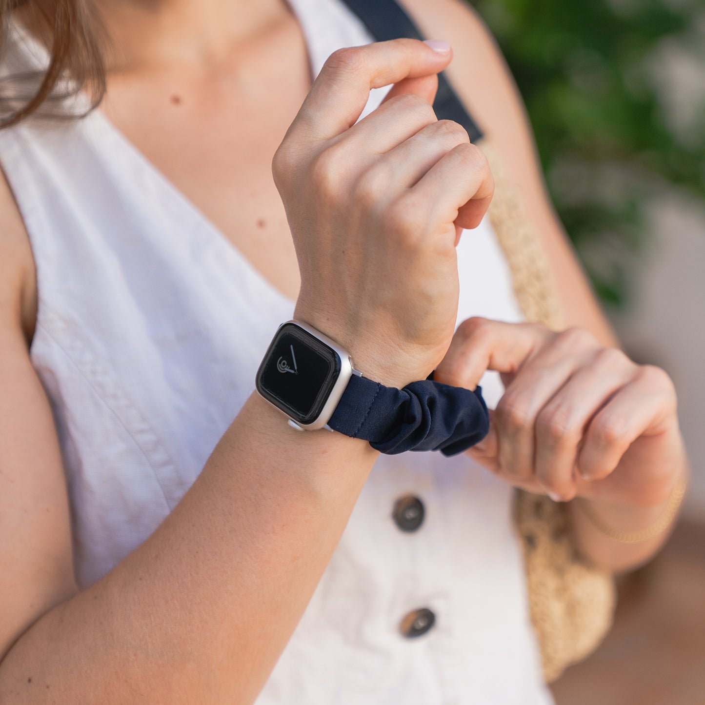 Eine Person in einem ärmellosen weißen Oberteil passt ein arktisband Apple Watch Scrunchie Armband "Elanora" - ein marineblaues, elastisches Scrunchie-Band von arktisband - an ihr Handgelenk an.