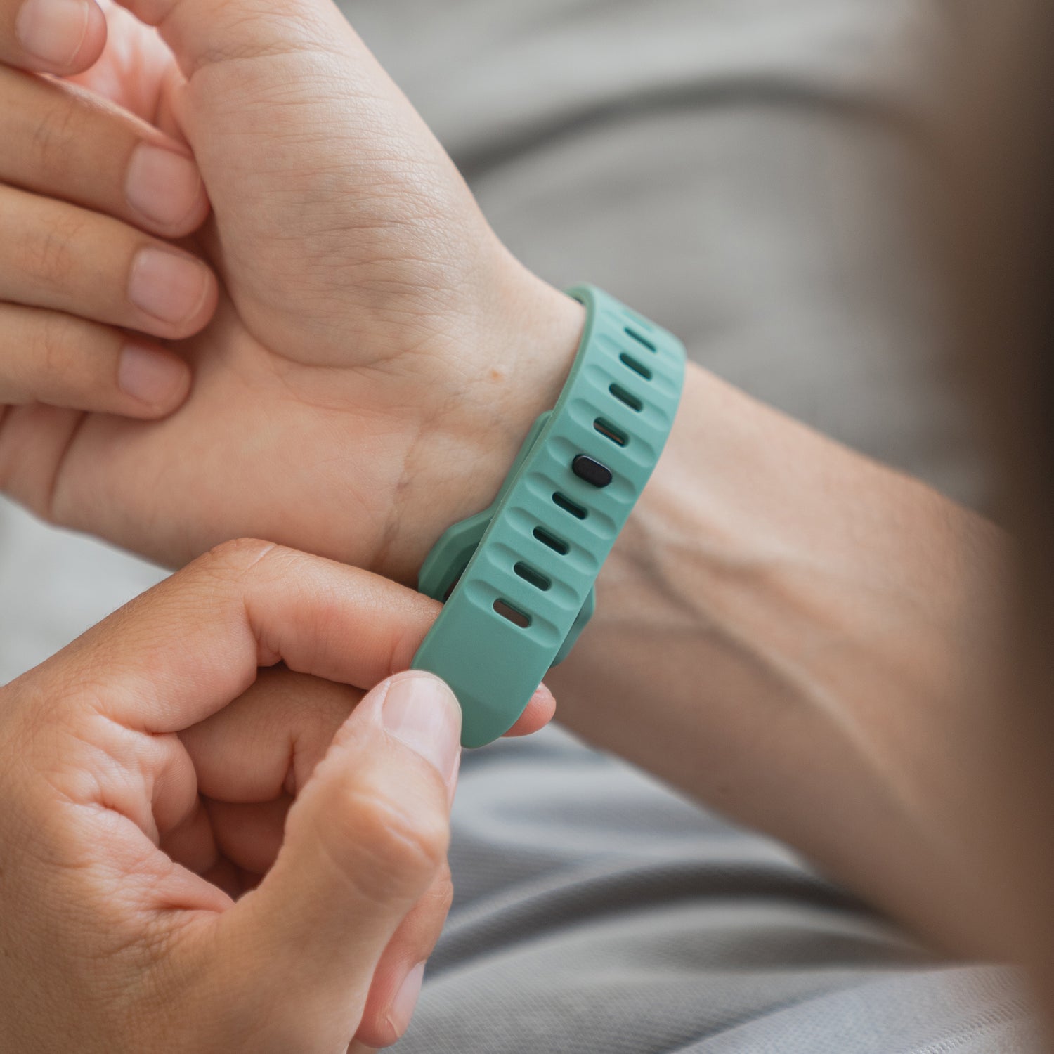 Jemand befestigt ein arktisband Apple Watch Silikonarmband "Active" in Türkis am Handgelenk eines anderen. Das arktisband verfügt über ein atmungsaktives Design, mehrere Größenanpassungslöcher und wird mit einer Hand befestigt, während das andere Handgelenk gestützt wird.