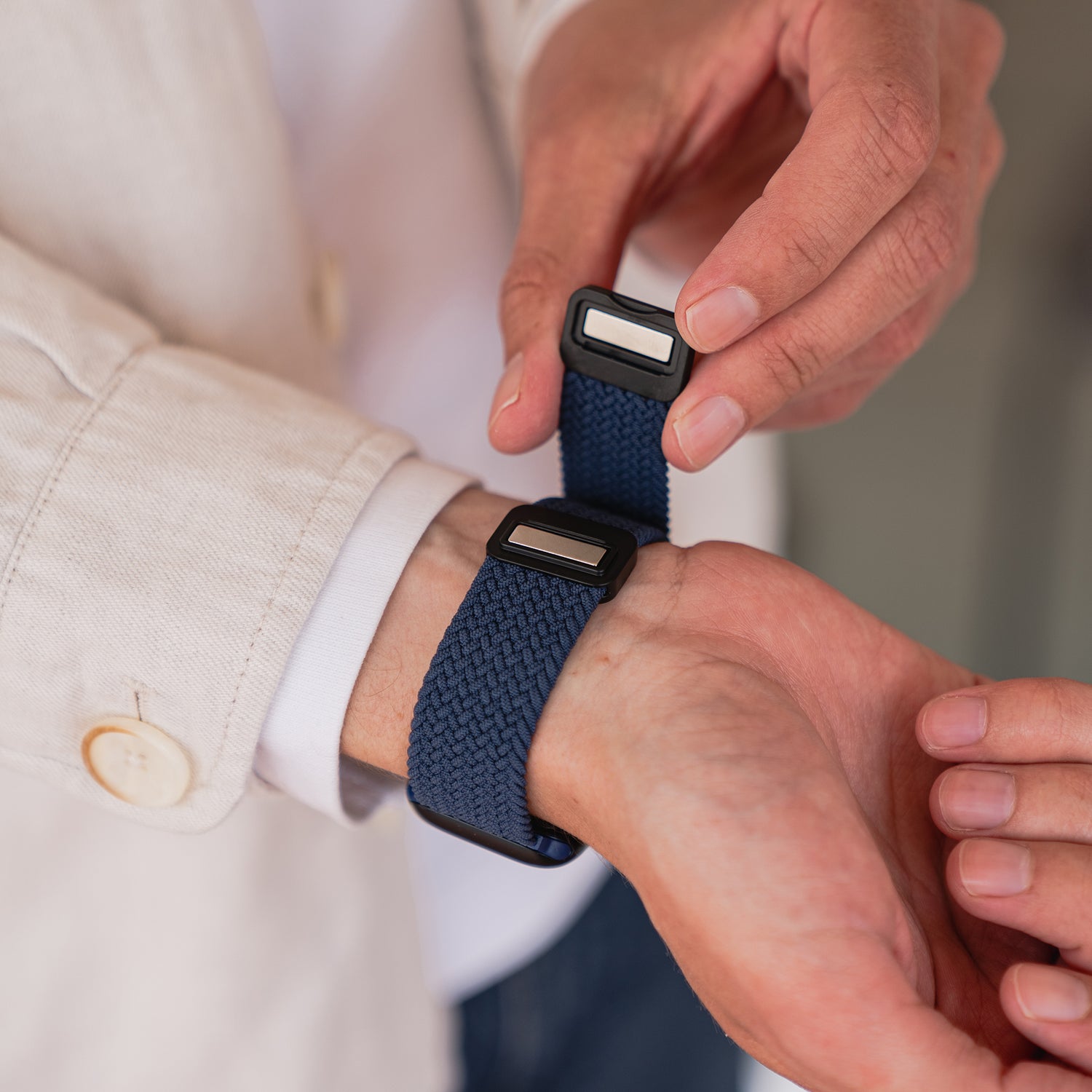 Jemand befestigt ein Arktisband Geflochtenes Apple Watch Armband „Casual“ mit Magnetverschluss in Marineblau um sein Handgelenk und trägt dabei eine helle Jacke.