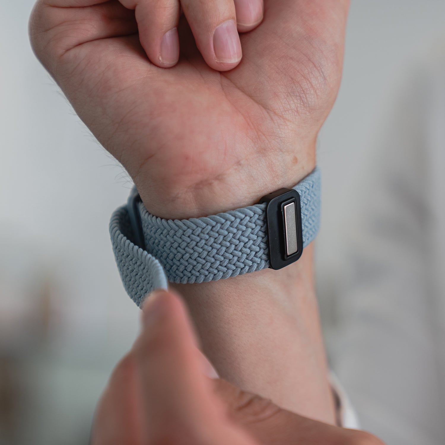 Man befestigt das hellblaue arktisband Geflochtene Apple Watch Armband „Casual“ von arktisband mit seinem rechteckigen schwarzen Magnetverschluss am Handgelenk.