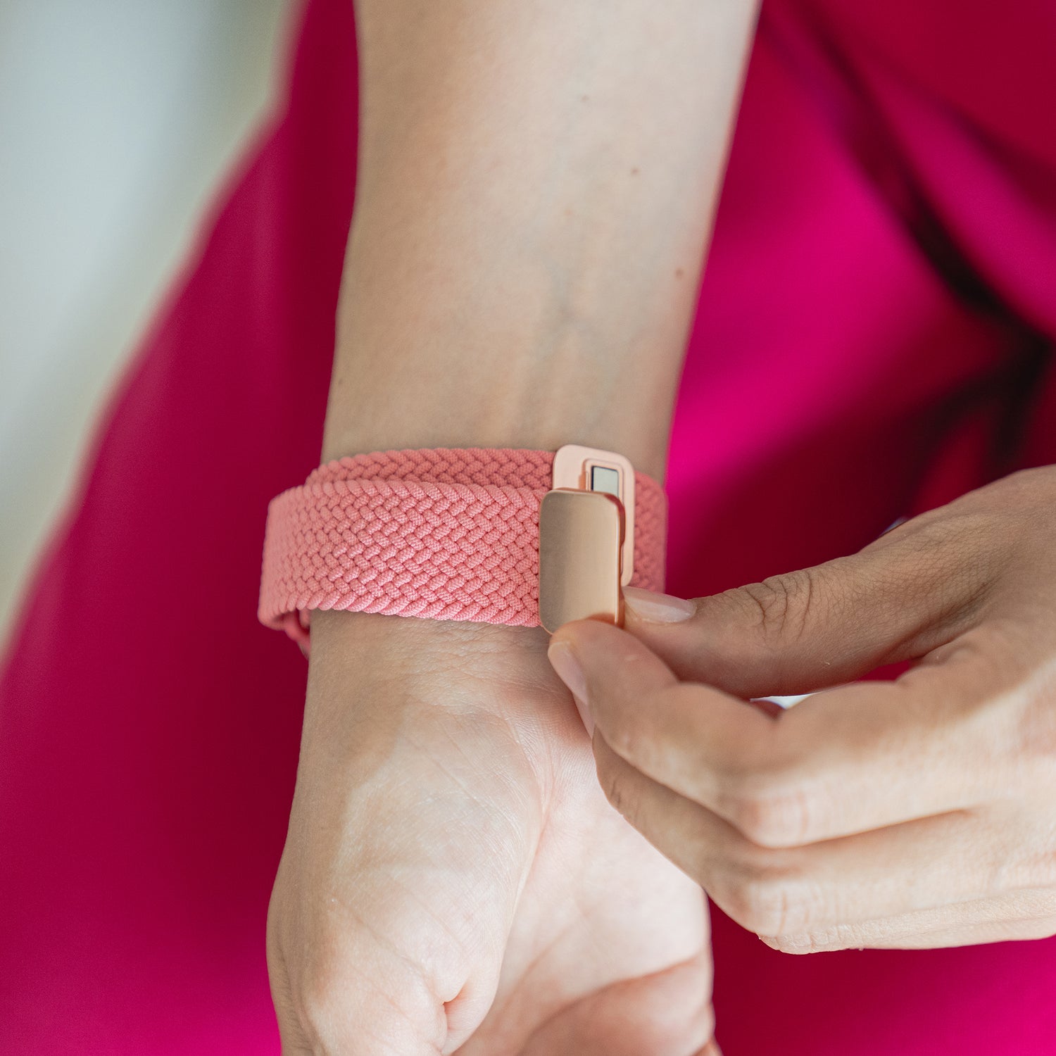 Eine Person befestigt ein arktisband Geflochtenes Apple Watch Armband „Casual“ mit Magnetverschluss um ihr Handgelenk, passend zu ihrem knallrosa Outfit.