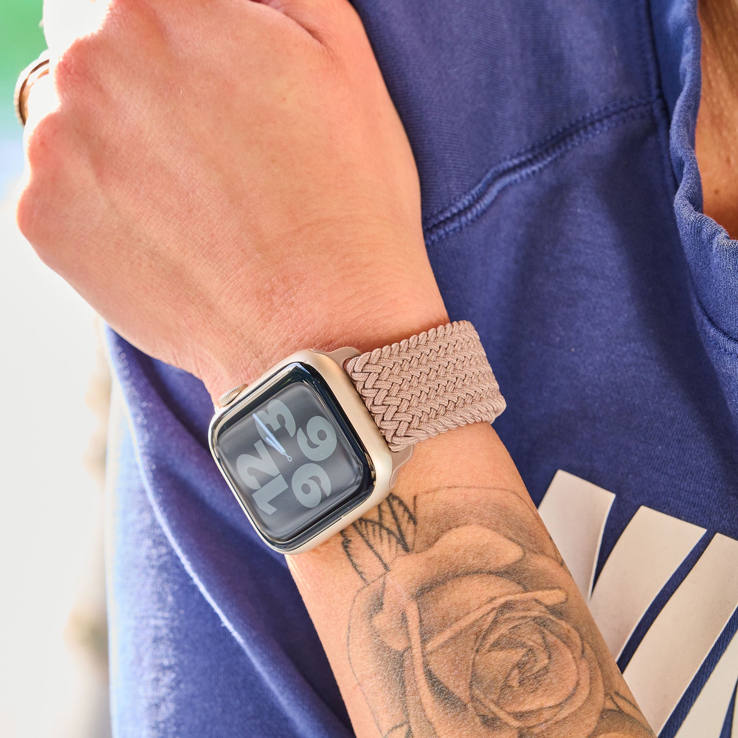 Eine Person trägt ein kunstvoll geflochtenes Apple Watch Armband „Casual“ mit Magnetverschluss und trägt ein Rosentattoo auf dem Unterarm.