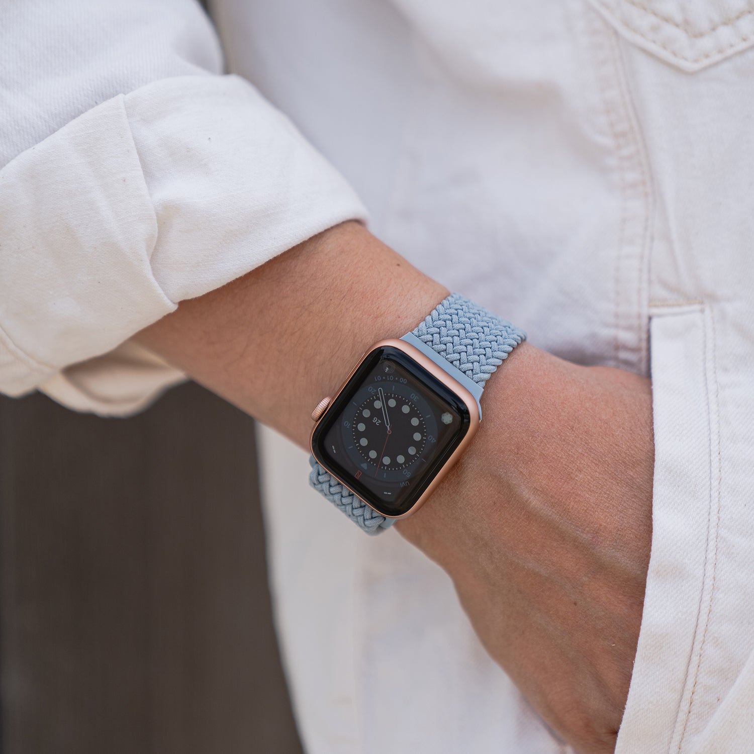 Eine Person trägt ein von Arktisband geflochtenes Apple Watch Armband „Casual“ mit Magnetverschluss in Hellblau mit weißer Hülle, die Hand in der Tasche.