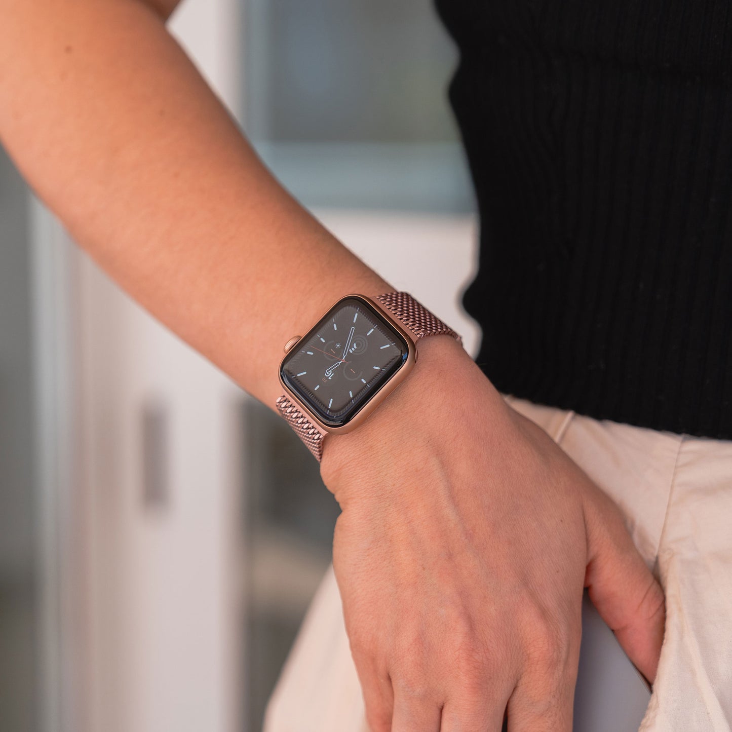 Eine Person in einem schwarzen ärmellosen Top und einem leichten Rock ist von der Taille abwärts zu sehen und trägt das arktisband Apple Watch Milanaise Armband „Bold“ in Roségold elegant am Handgelenk.