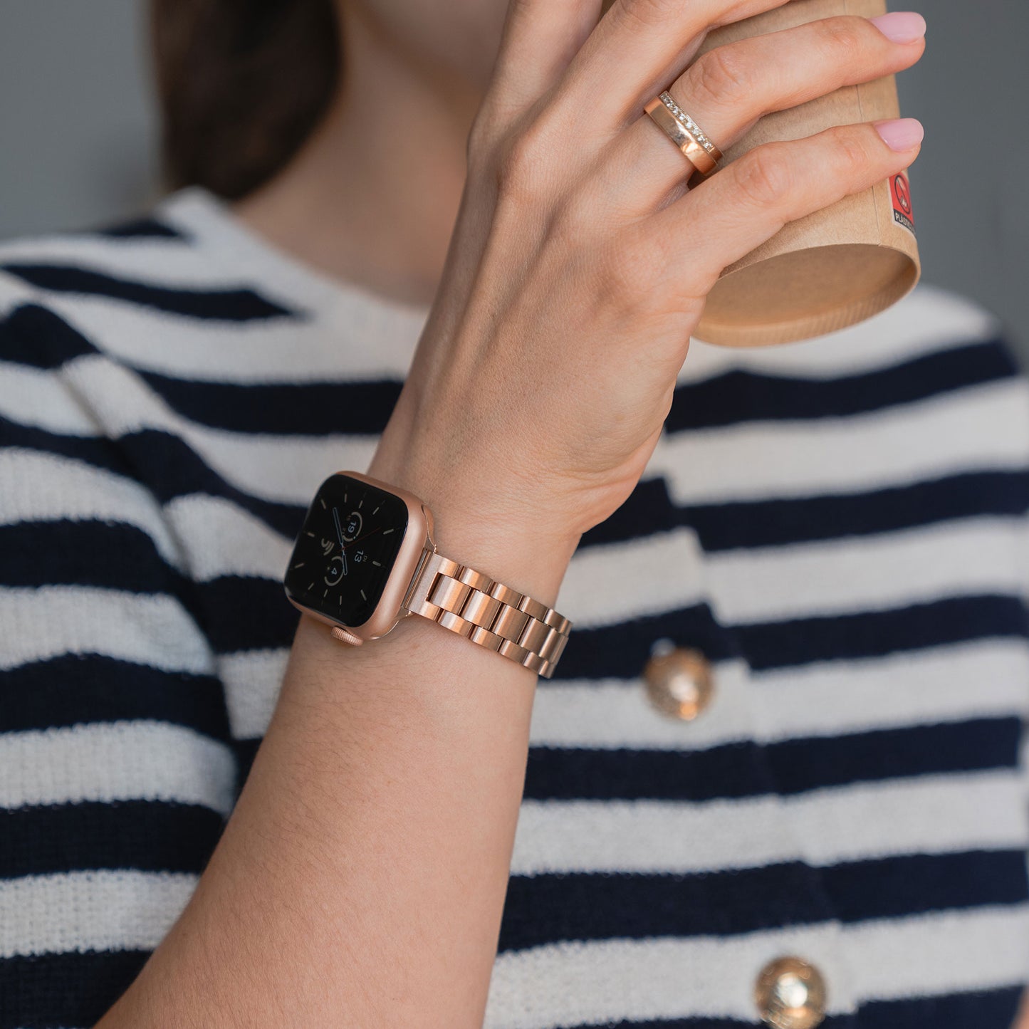 Eine Person im gestreiften Hemd trägt das arktisband Apple Watch Gliederarmband „Arctica“ – Slim von arktisband und hält einen Pappbecher an den Mund.