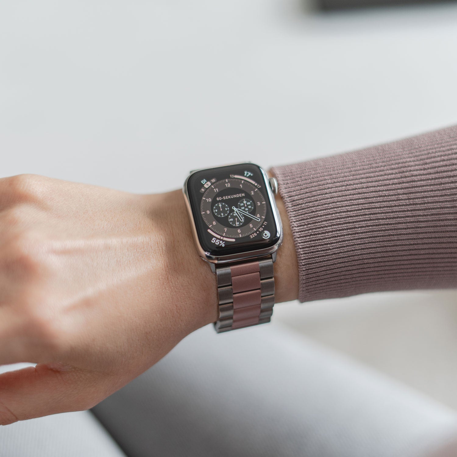 Eine Person trägt das arktisband Apple Watch Gliederarmband „Arctica“ von arktisband mit dunklem Ziffernblatt. Sie trägt ein malvenfarbenes Langarmshirt und ihre Hände sind entspannt und leicht zur Faust geballt.