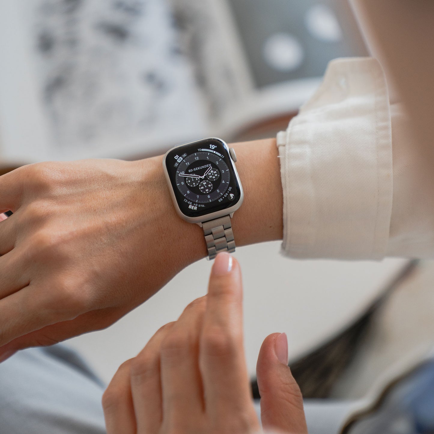 Man tippt auf das arktisband Apple Watch Gliederarmband „Arctica“ – Slim mit rundem, schwarzem Display. Das elegante Edelstahlarmband von arktisband zeigt die Uhrzeit und weitere Details auf dem Zifferblatt an.