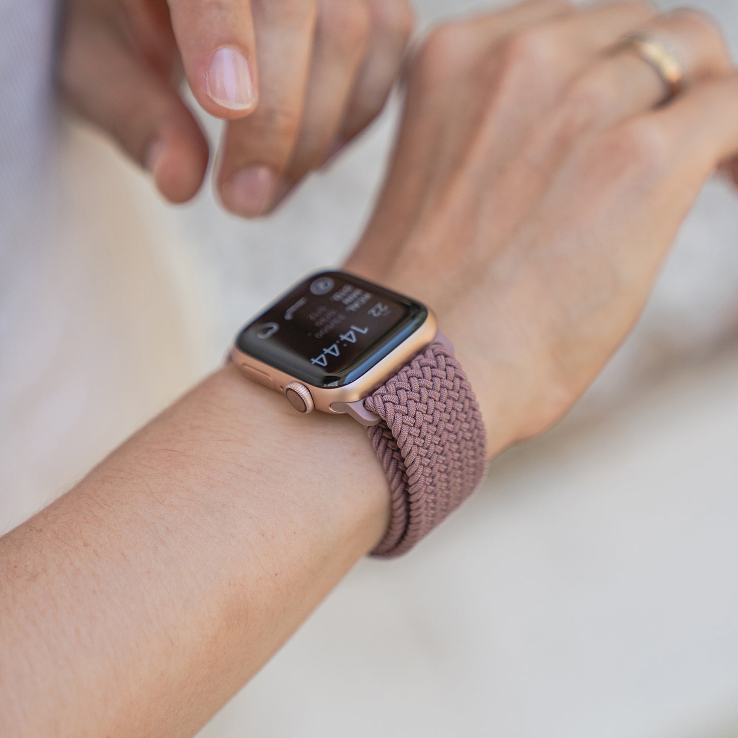 Nahaufnahme einer Person, die ein kunstvoll geflochtenes Apple Watch Armband „Casual“ mit Magnetverschluss in Lila an ihrem Handgelenk anpasst.