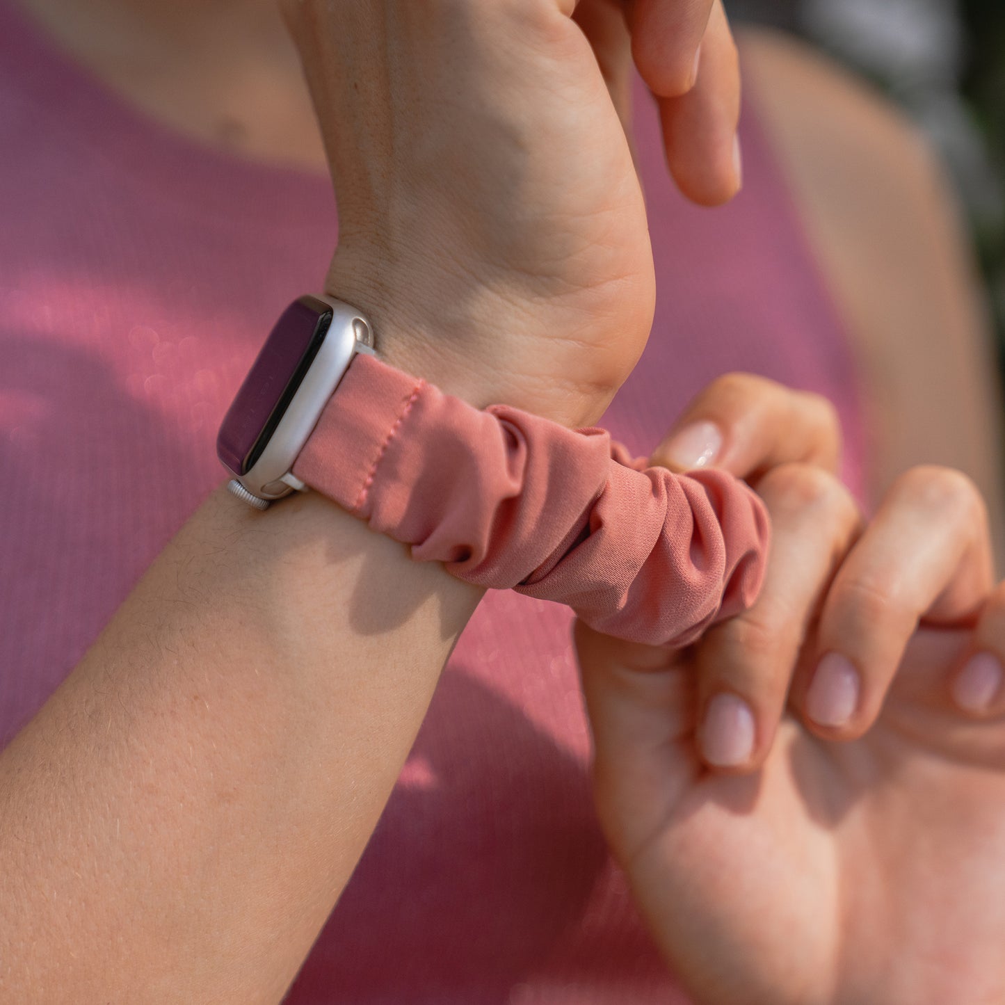 Nahaufnahme einer Person, die das arktisband Apple Watch Scrunchie Armband "Elanora", ein rosa Gummiband von arktisband, an ihrem Handgelenk anpasst.