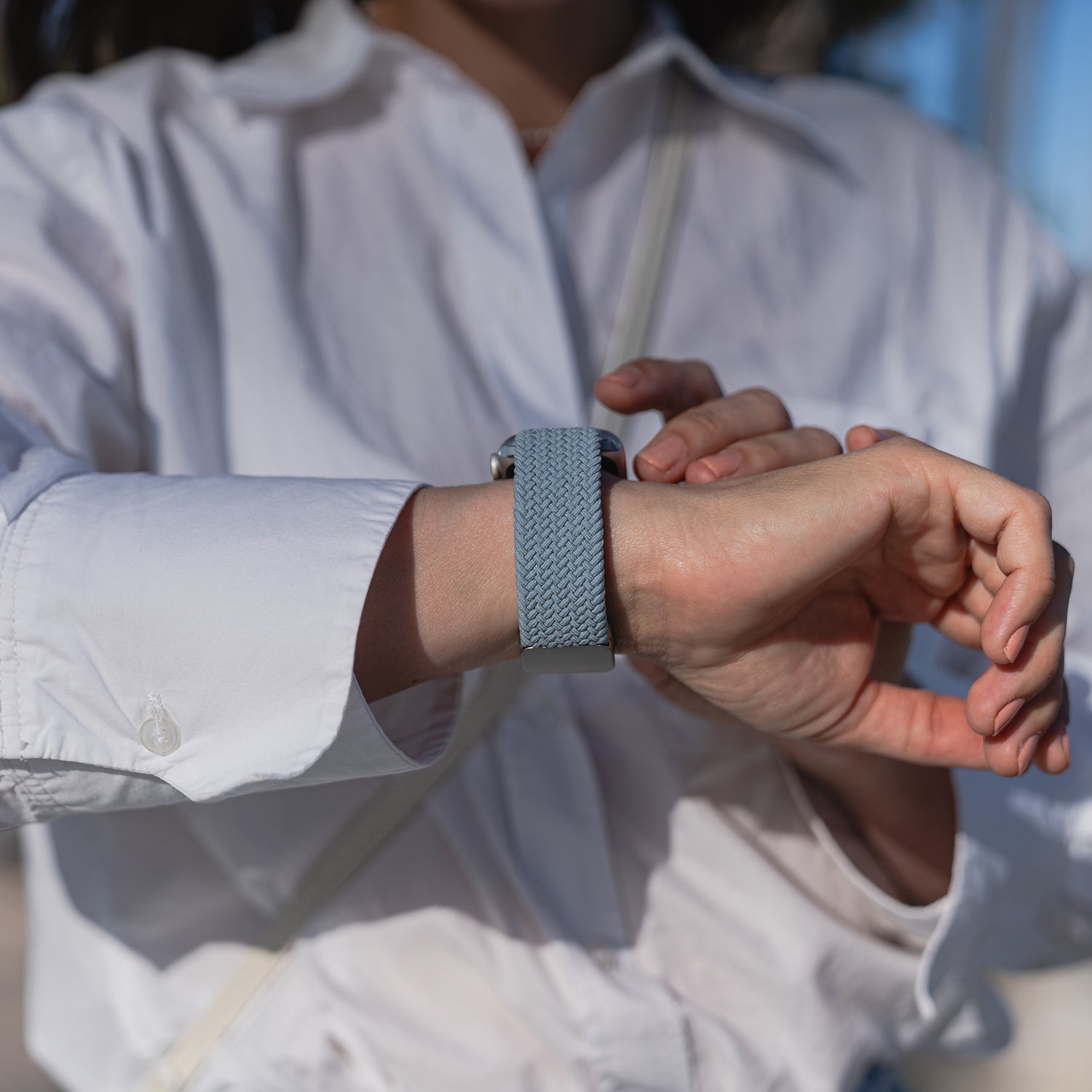 Person im weißen Hemd richtet im Freien ein mit Arktisband geflochtenes Apple Watch Armband „Casual“ mit Magnetverschluss in Hellblau.