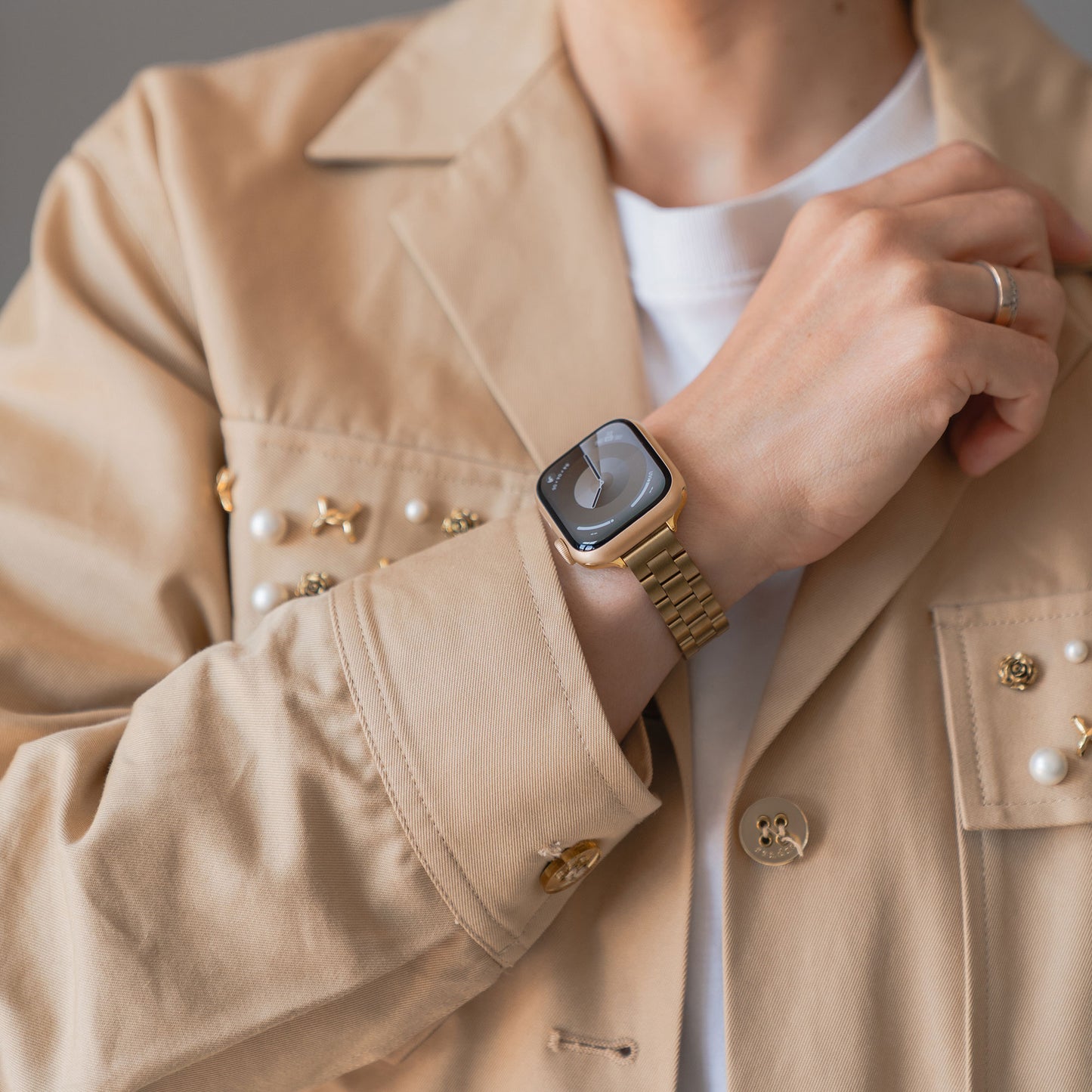 Eine Person trägt eine beige Jacke mit Perlenakzenten und ein elegantes arktisband Apple Watch Gliederarmband „Arctica“ – Slim von arktisband am Handgelenk.