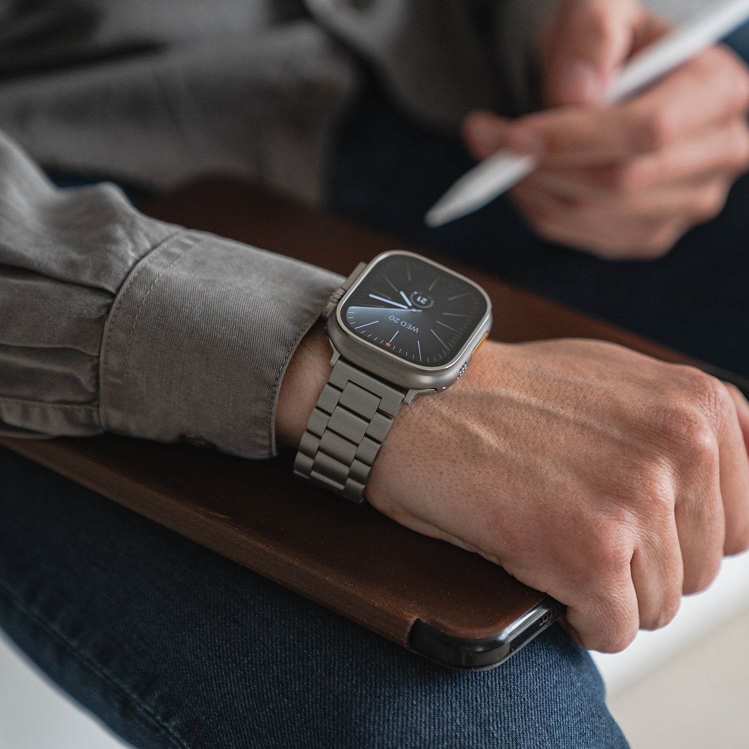Eine Person, die das Arktisband Apple Watch Gliederarmband „Arctica“ trägt, legt ihre Hand auf ein dunkles Tablet, hält einen Stift und trägt ein graues Hemd und blaue Jeans.