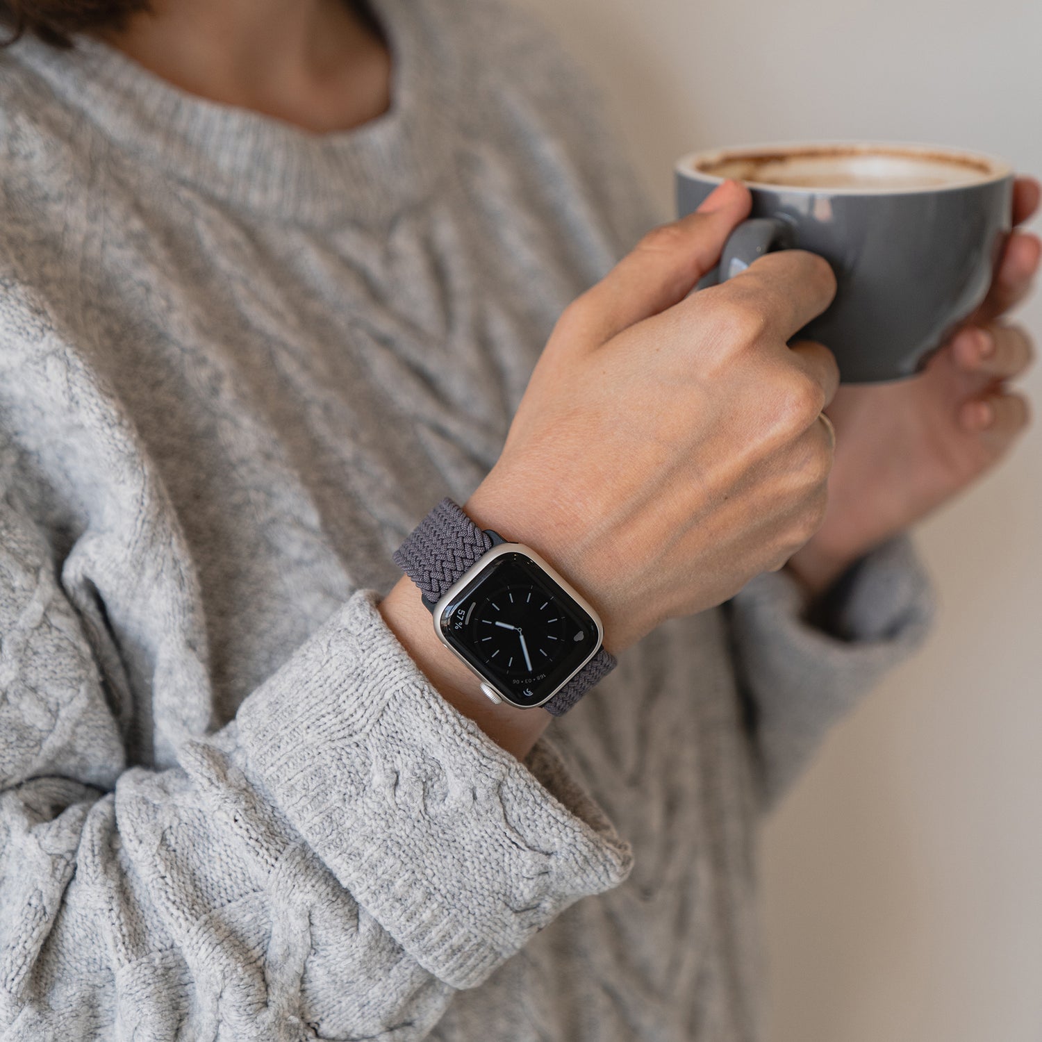 Eine Person in einem grauen Pullover hält eine Tasse in der Hand und trägt das geflochtene Apple Watch Armband „Casual“ mit Magnetverschluss von arktisband.