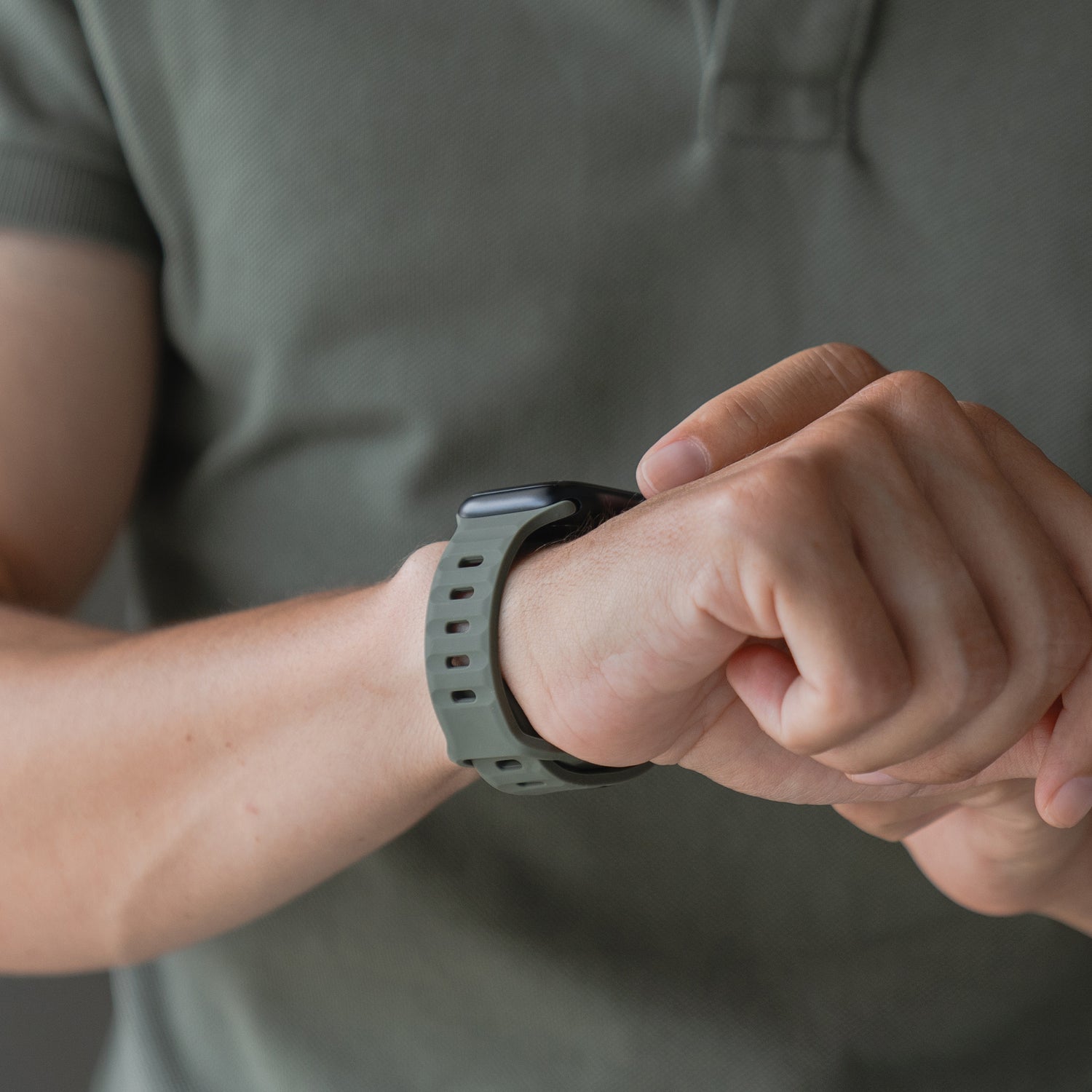 Eine Person in einem grünen Kurzarmshirt rückt ein Arktisband Apple Watch Silikonarmband „Active“ mit grünem Band an ihrem linken Handgelenk zurecht; sichtbar sind lediglich Oberkörper und Hände.