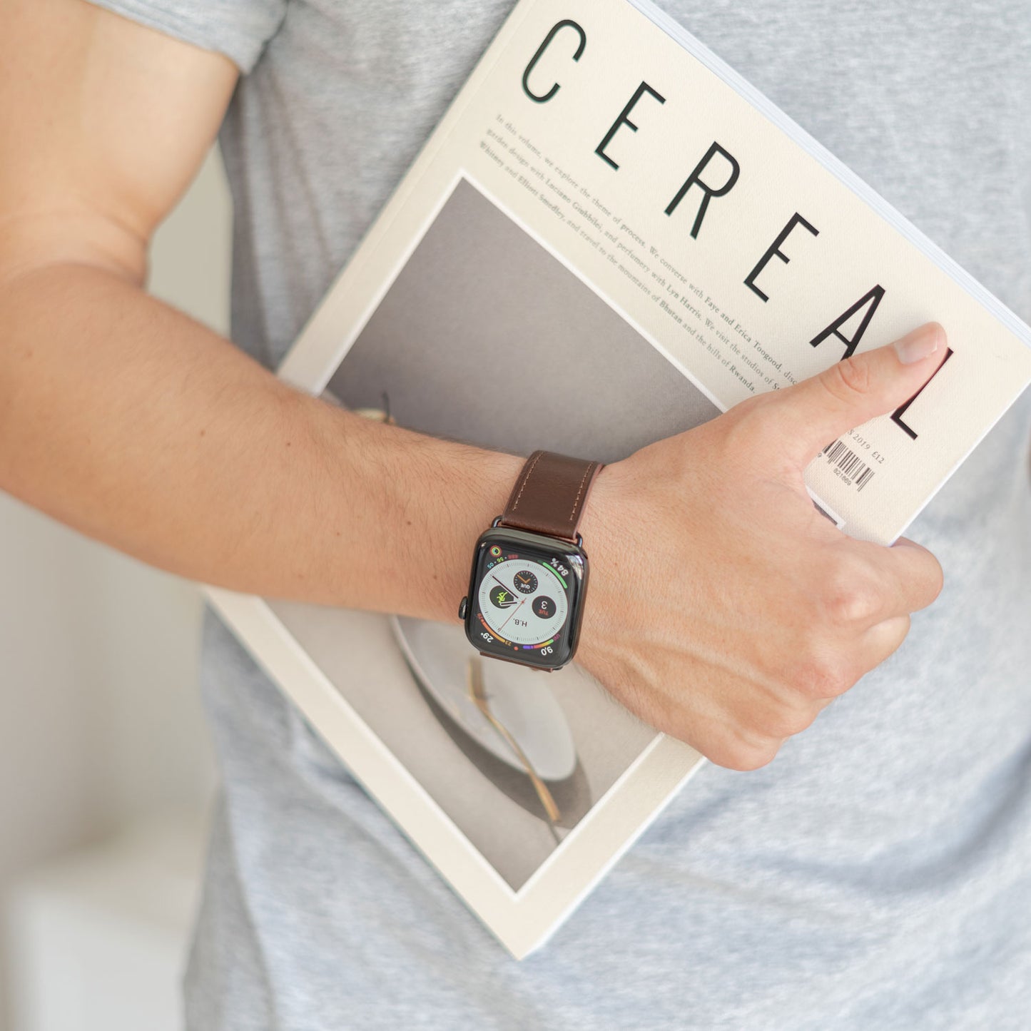Jemand trägt ein graues T-Shirt und eine Apple Watch mit dem arktisband „Premium“-Lederarmband von arktisband und hält eine Zeitschrift mit dem Titel CEREAL unter dem Arm.