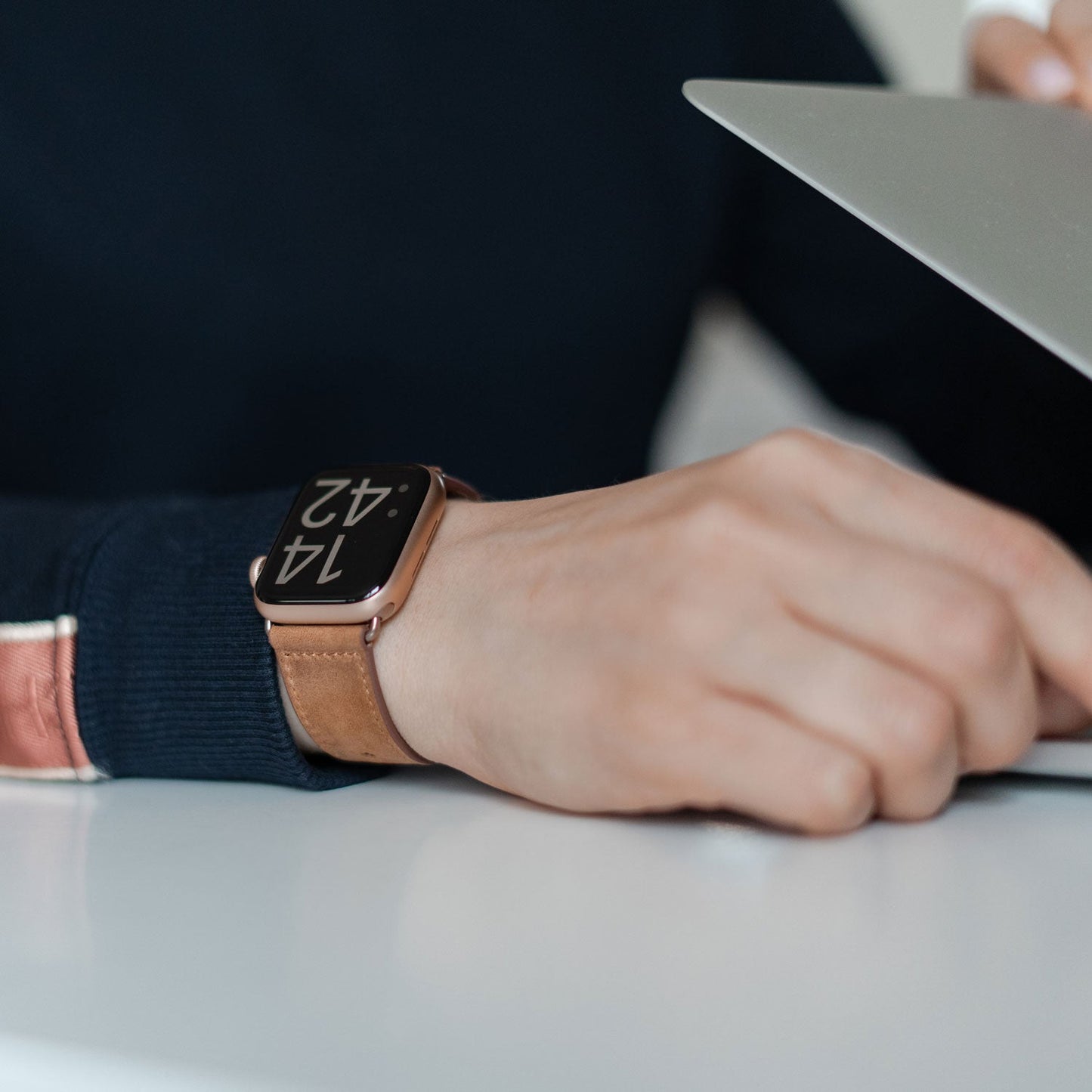 Eine Person, die das arktisband Apple Watch Kunstlederarmband von arktisband, bekannt für maximalen Tragekomfort, trägt, arbeitet an einem Laptop an einem weißen Schreibtisch, der einen minimalistischen Look unterstreicht.