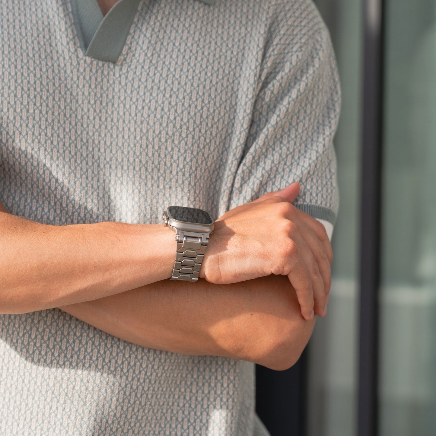 Person mit verschränkten Armen, die ein gemustertes Kurzarmhemd und das silberne Apple Watch-Armband Arktisband TXR-500 mit Schmetterlingsverschluss trägt.