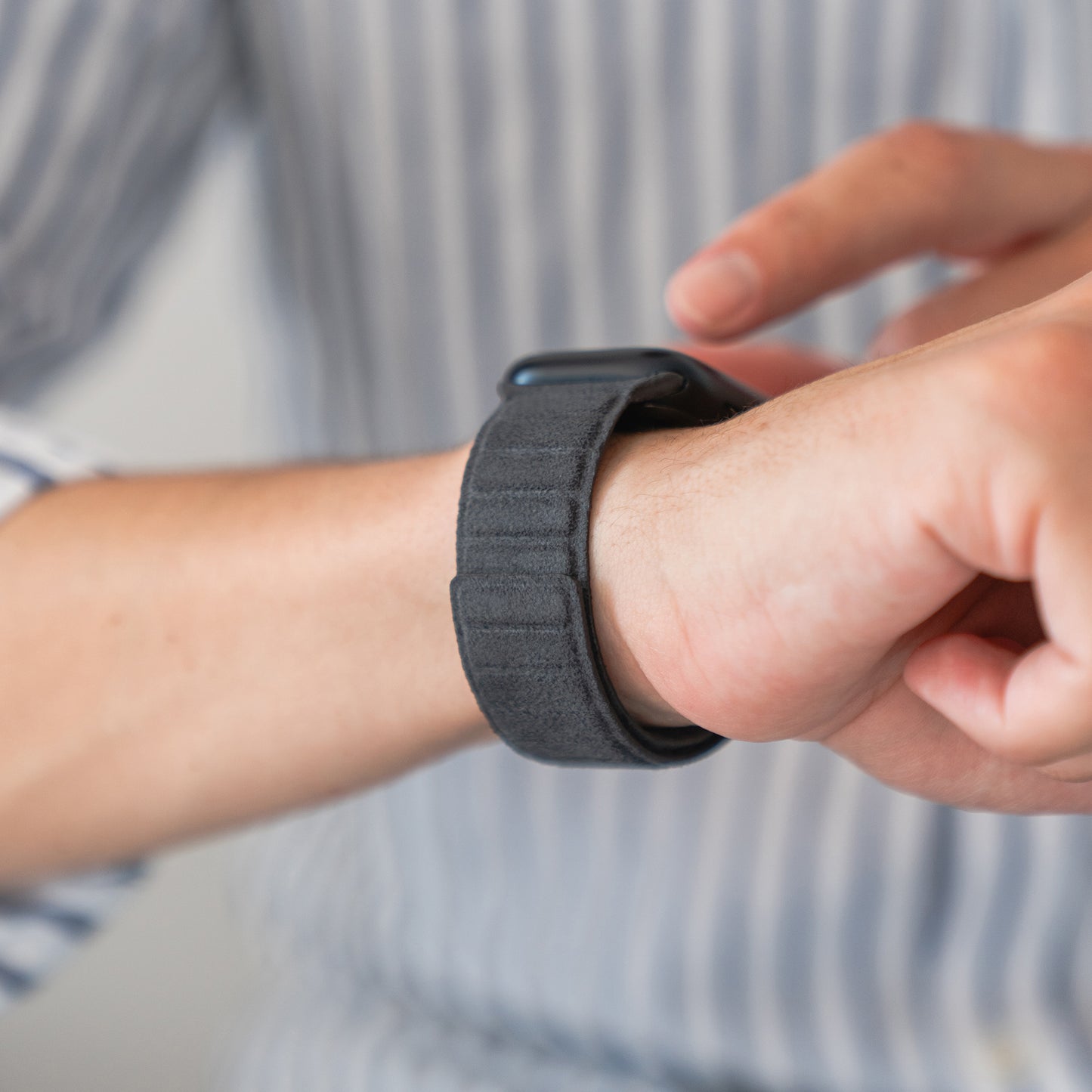 Eine Person in einem gestreiften Hemd trägt eine Apple Watch von arktisband magnetisches Armband aus Alcantara und berührt den Bildschirm ihrer Smartwatch.