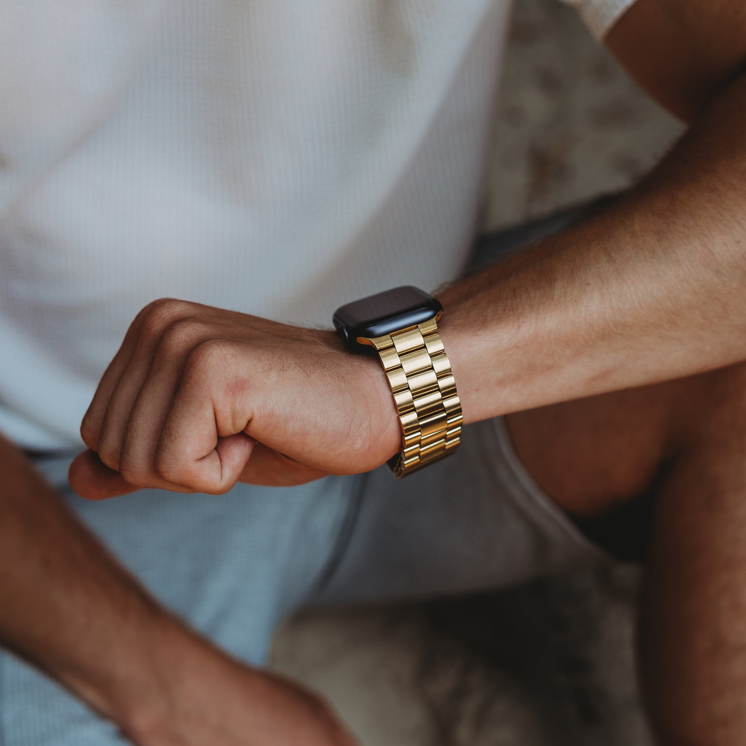 Eine Person trägt ein arktisband Apple Watch Gliederarmband „Arctica“ von arktisband am Handgelenk, ist mit einem weißen Shirt und hellblauen Shorts bekleidet, hat den Arm angewinkelt und die Faust leicht geballt.